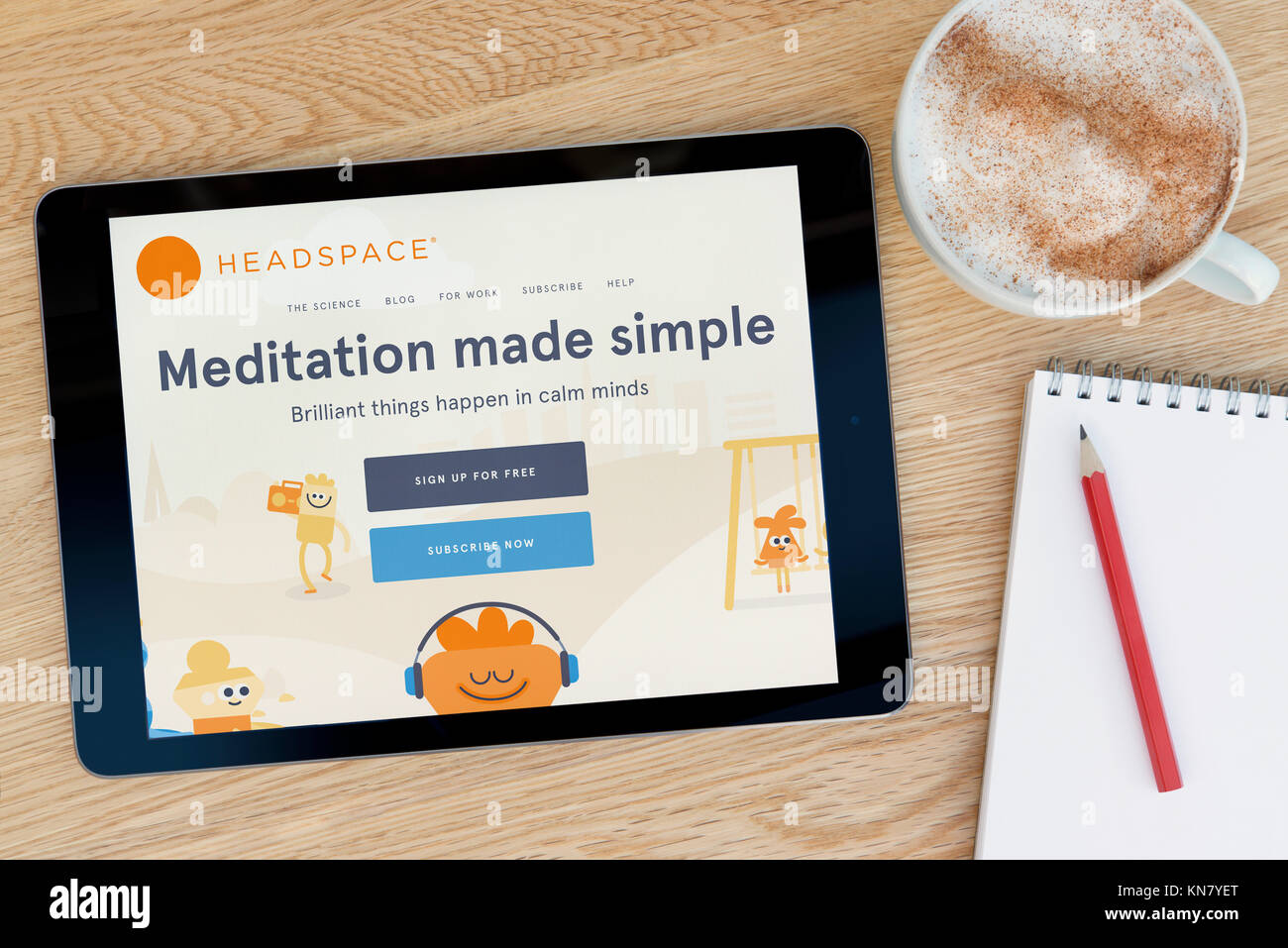 The Headspace meditation website on an iPad tablet device which rests on a wooden table beside a notepad and pencil & a cup of coffee -Editorial only Stock Photo