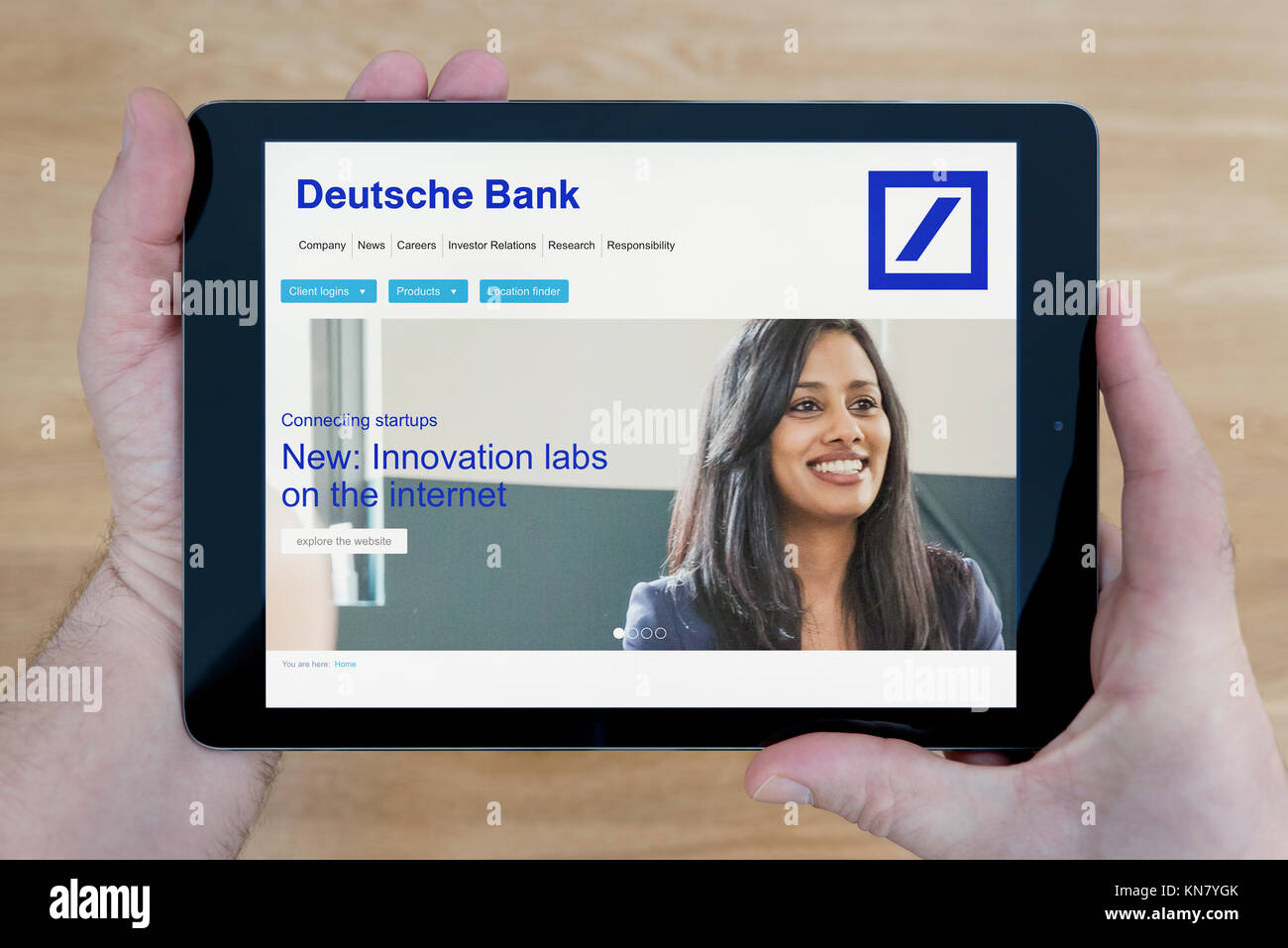 A man looks at the Deutsche Bank website on his iPad tablet device, shot against a wooden table top background (Editorial use only) Stock Photo