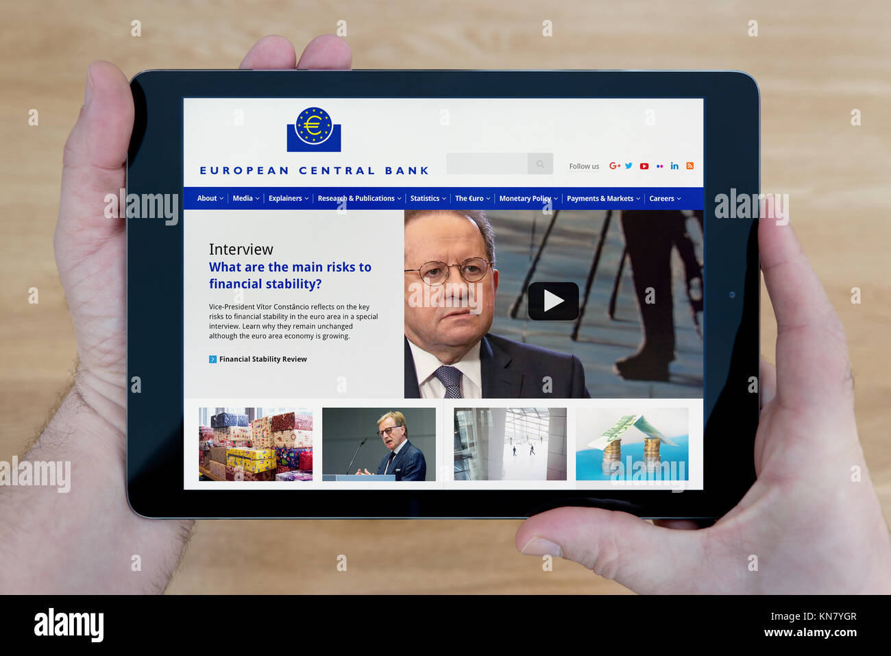 A man looks at the European Central Bank website on his iPad tablet device, shot against a wooden table top background (Editorial use only) Stock Photo