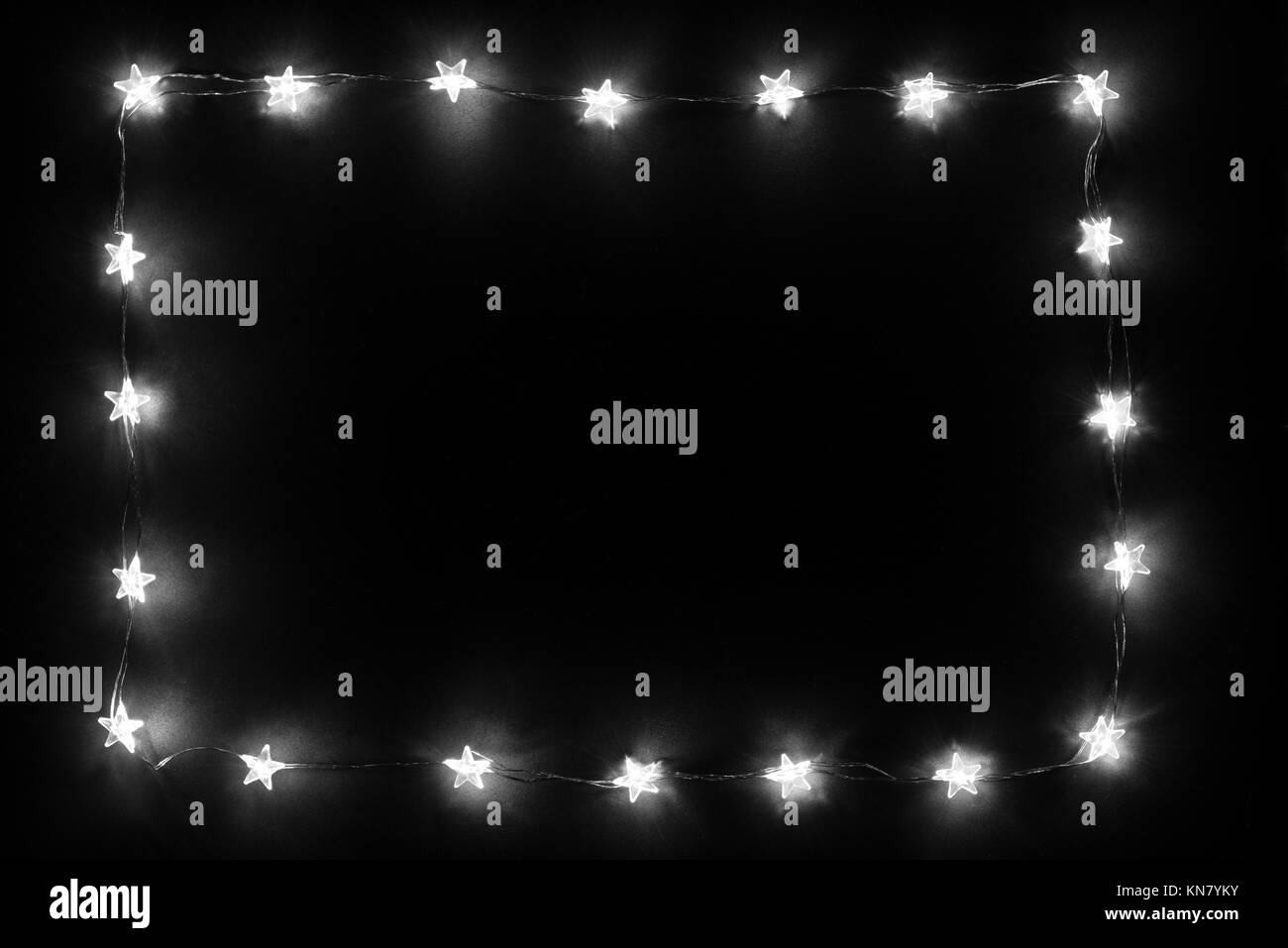 Glowing white Christmas ligth garland frame on dark black plaster background. Stock Photo