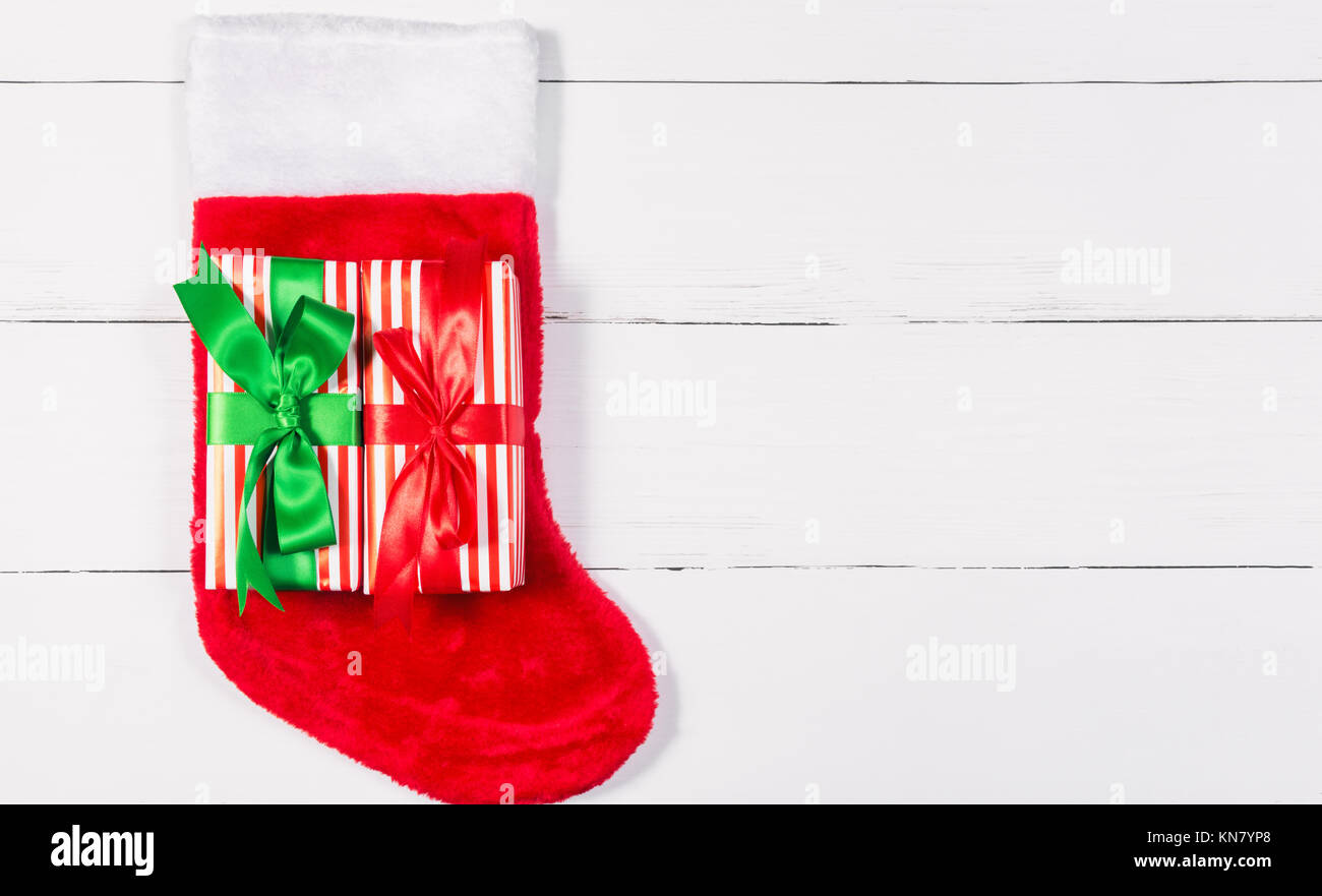 Giftwrapped Presents lying on Christmas Stocking on White Wooden Table Stock Photo