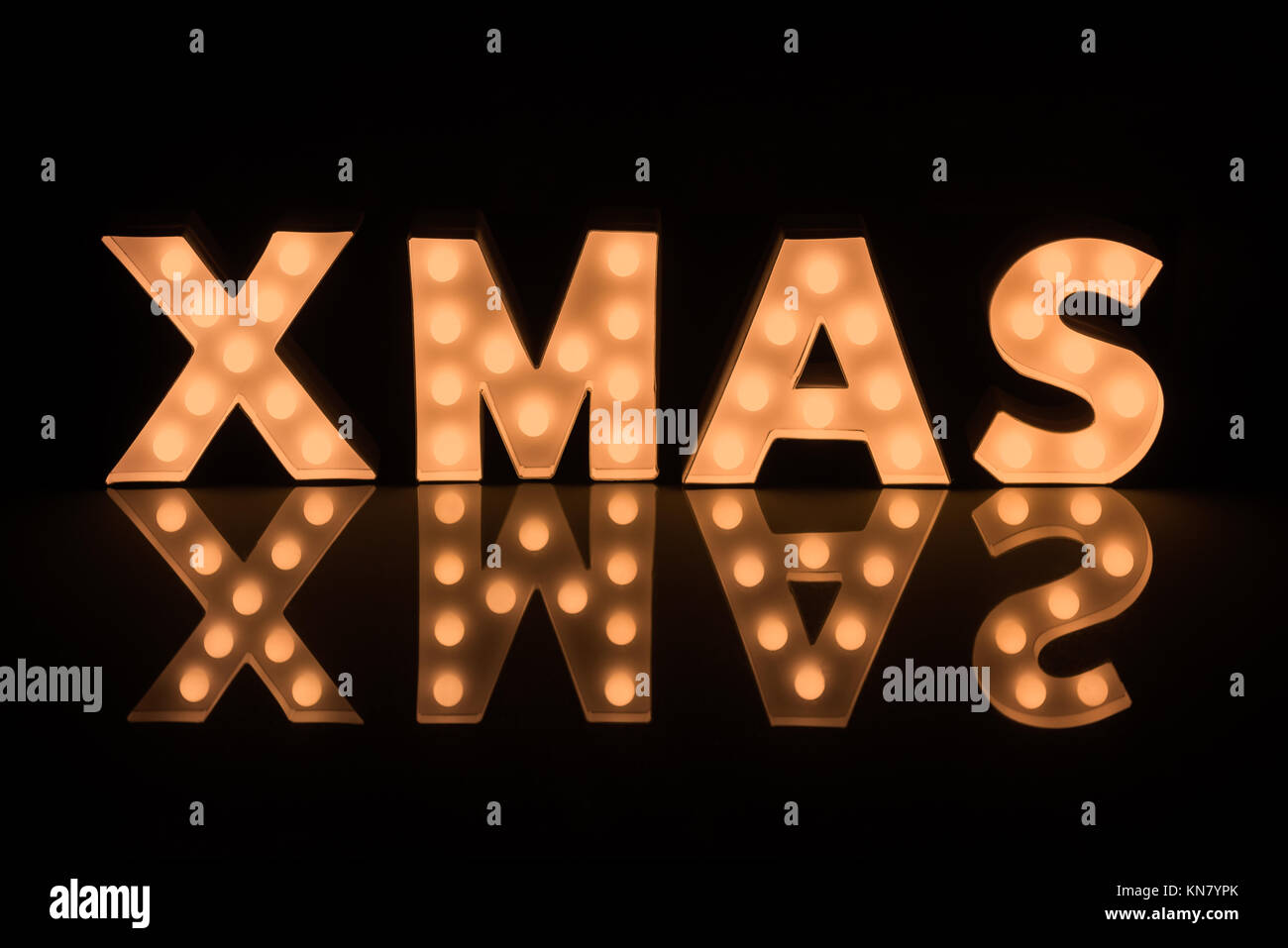 Illuminating Xmas Letters against dark background reflecting on Glass Surface Stock Photo