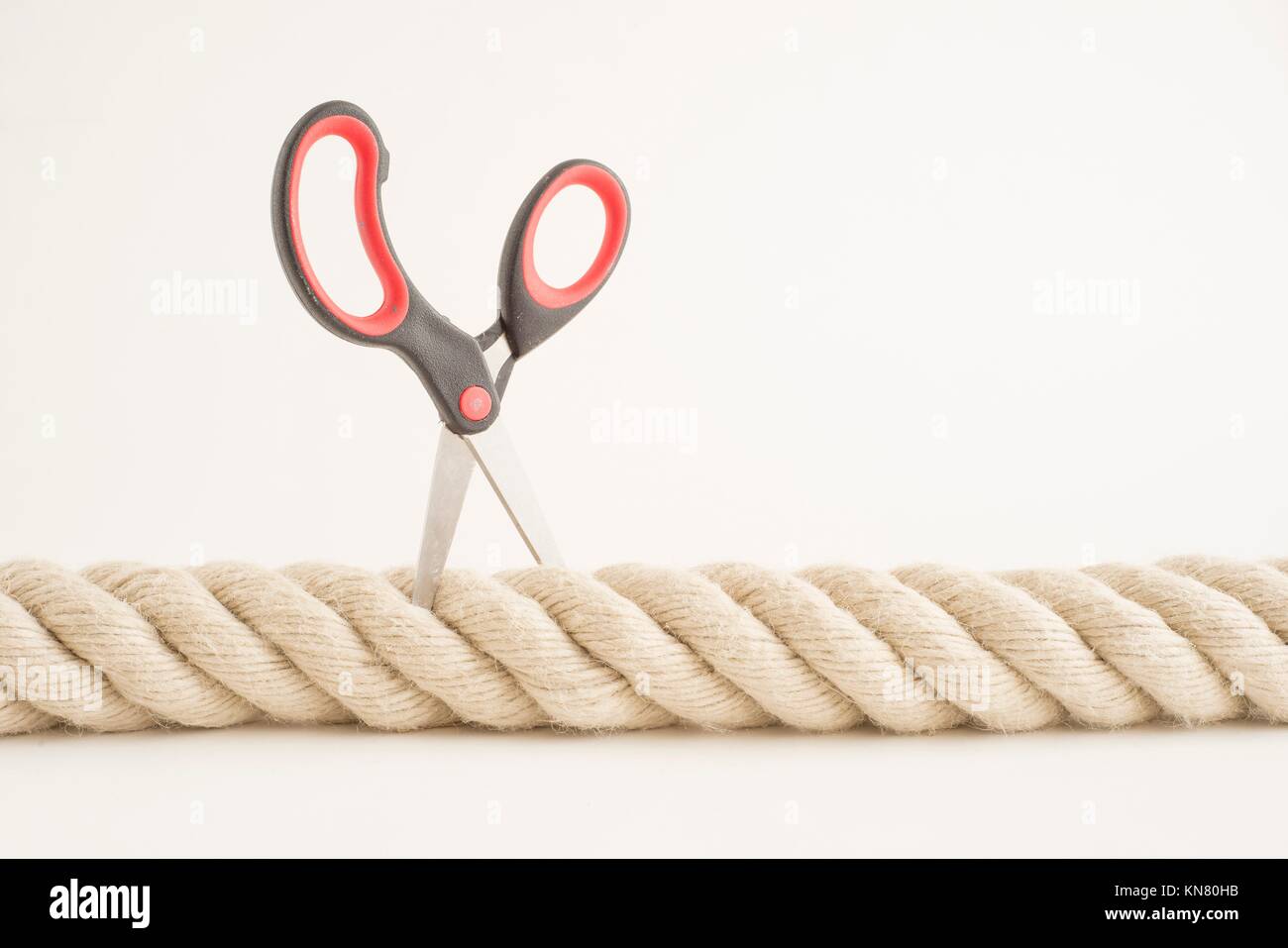 Cutting A Rope With Scissors Against White Background Stock Photo