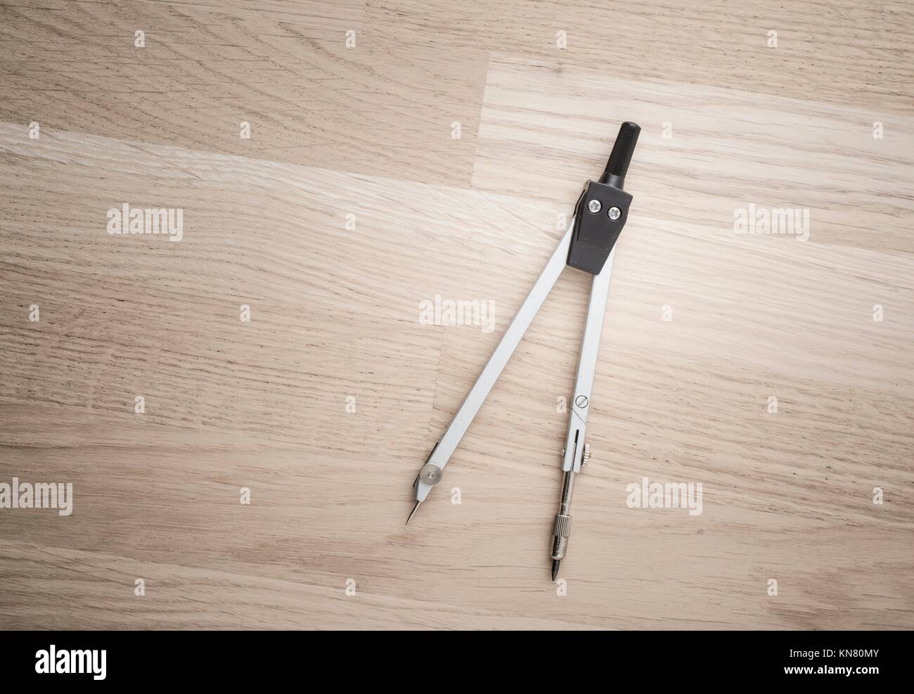 Compass used for design work or architecture lying on wooden desktop. Concept of geometry, drafting or construction planning. Stock Photo