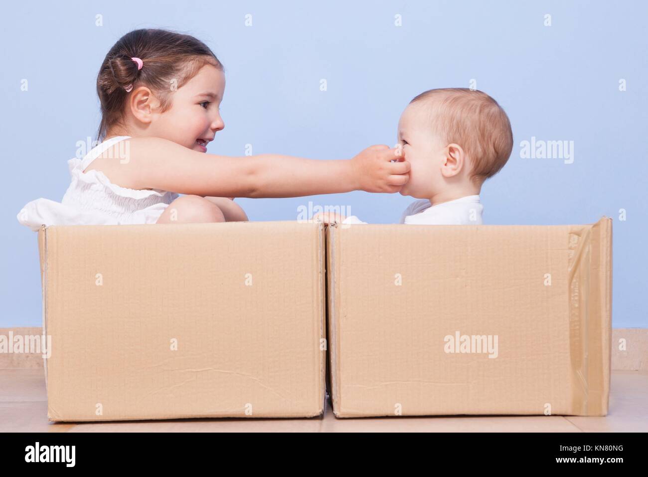 Baby brother and toddler sister playing in cardboard boxes. Stock Photo