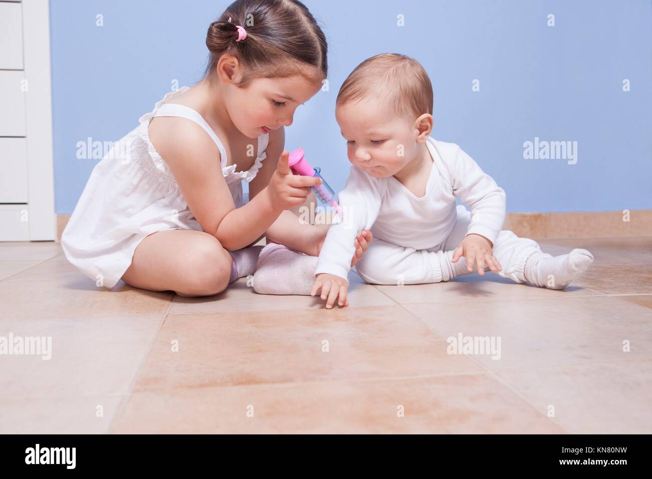Baby brother and toddler sister playing doctor with syringe. Stock Photo