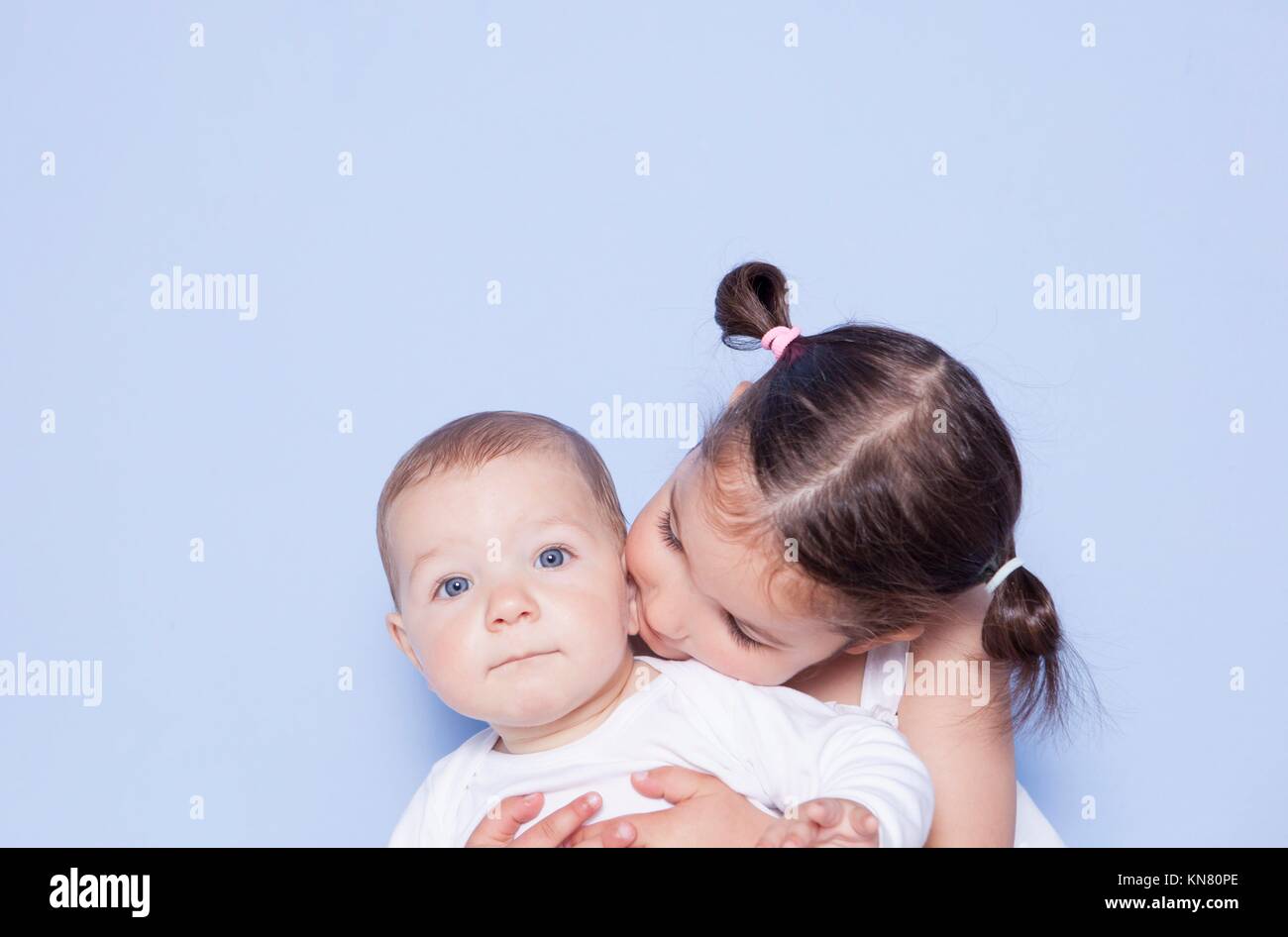 Little cute girl hugging little baby brother. Isolated over blue background. Stock Photo