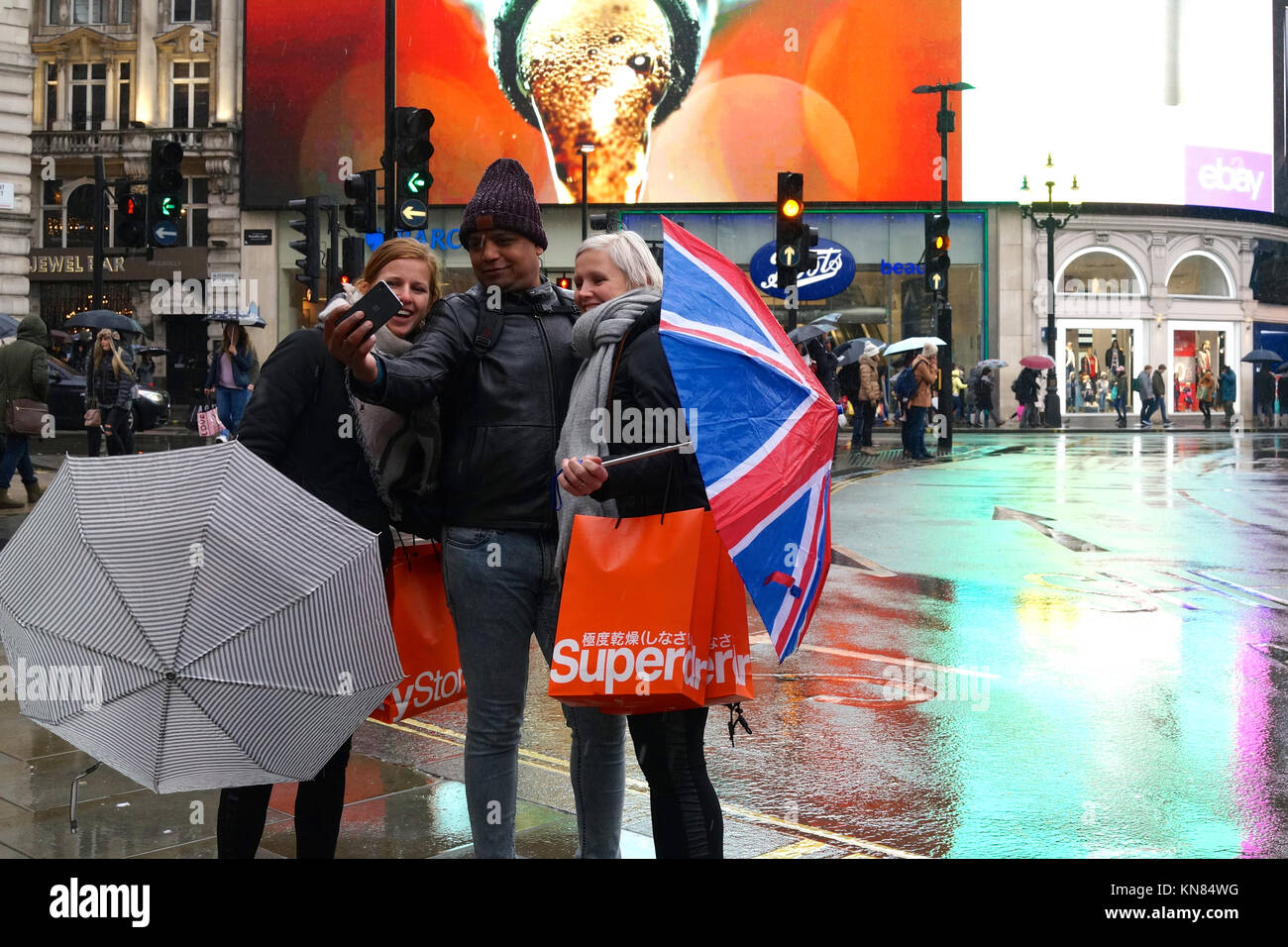 London in the rain: tourists smile for a selfie at Piccadily Circus Stock Photo