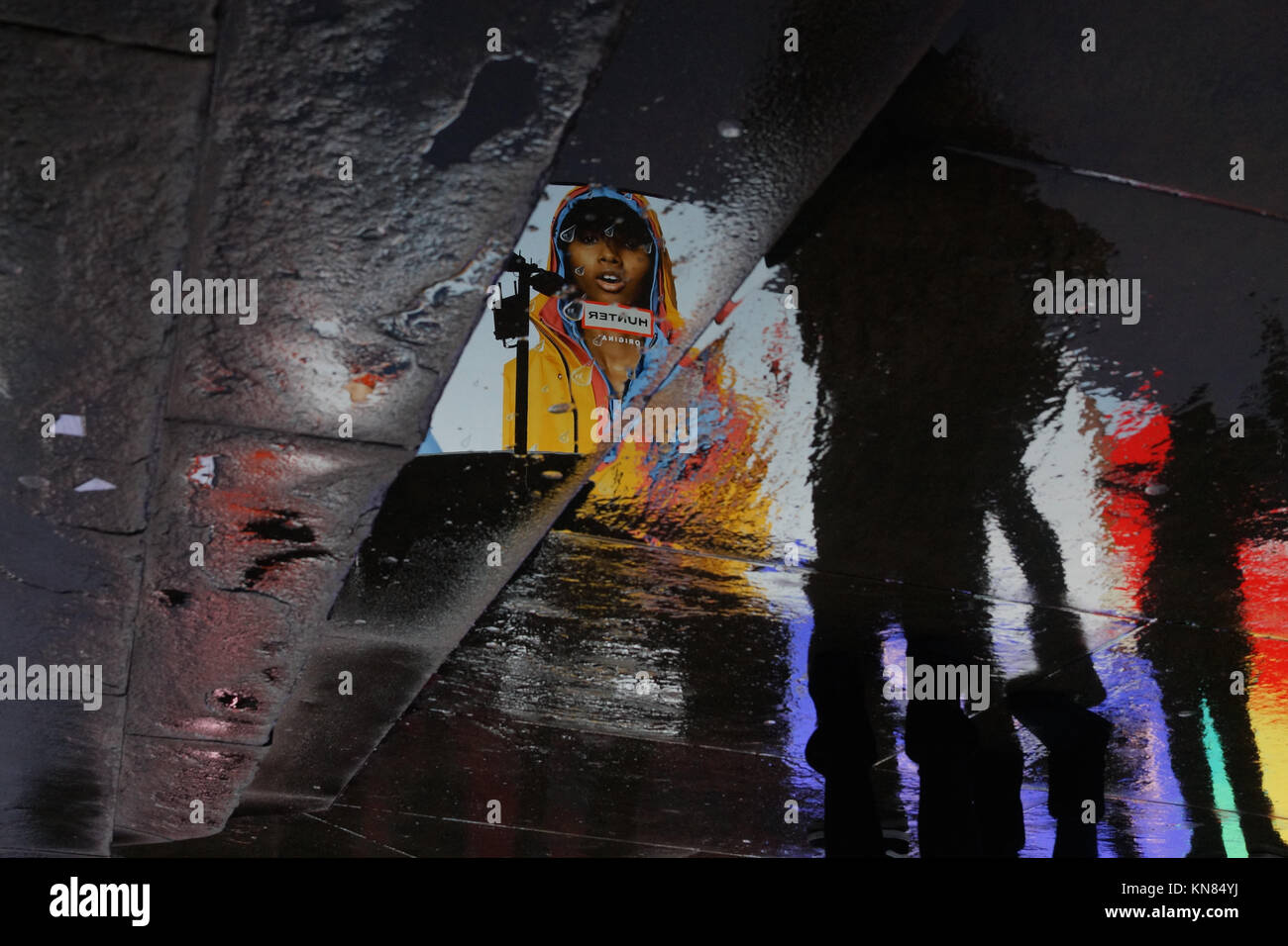London rain - a model in a waterproof coat reflected on a wet pavement at Piccadilly Circus Stock Photo