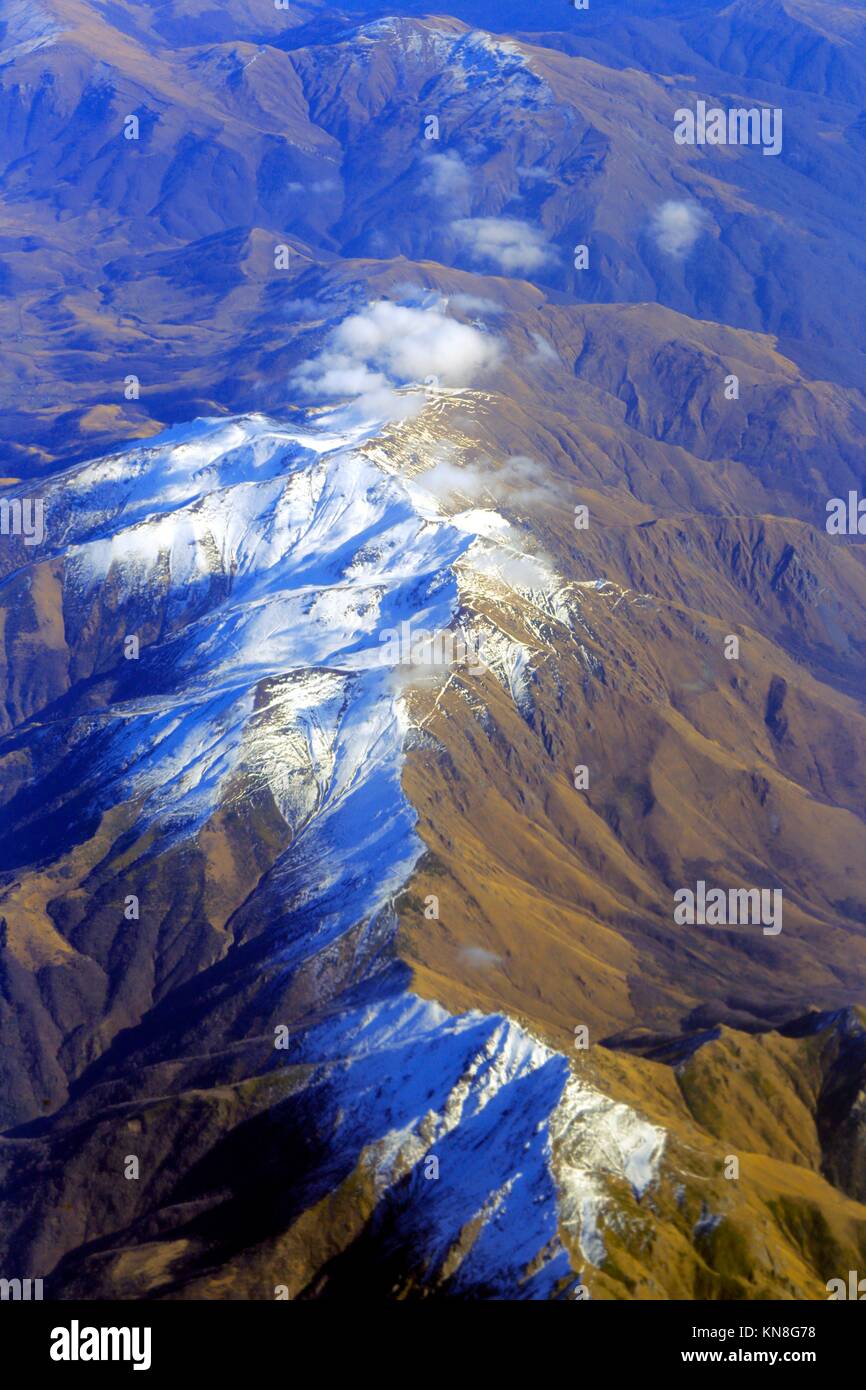 Aerial view of mountain peaks from airplane clouds sky. Stock Photo