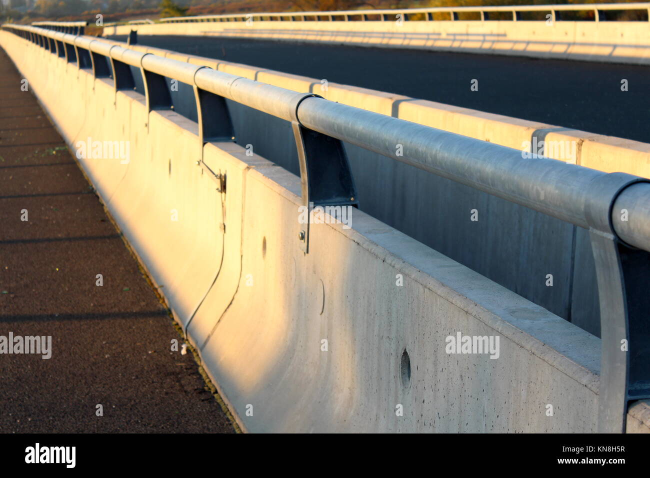 Concrete road bridge barrier with strong metal safety guard rails mounted on top at sunset Stock Photo