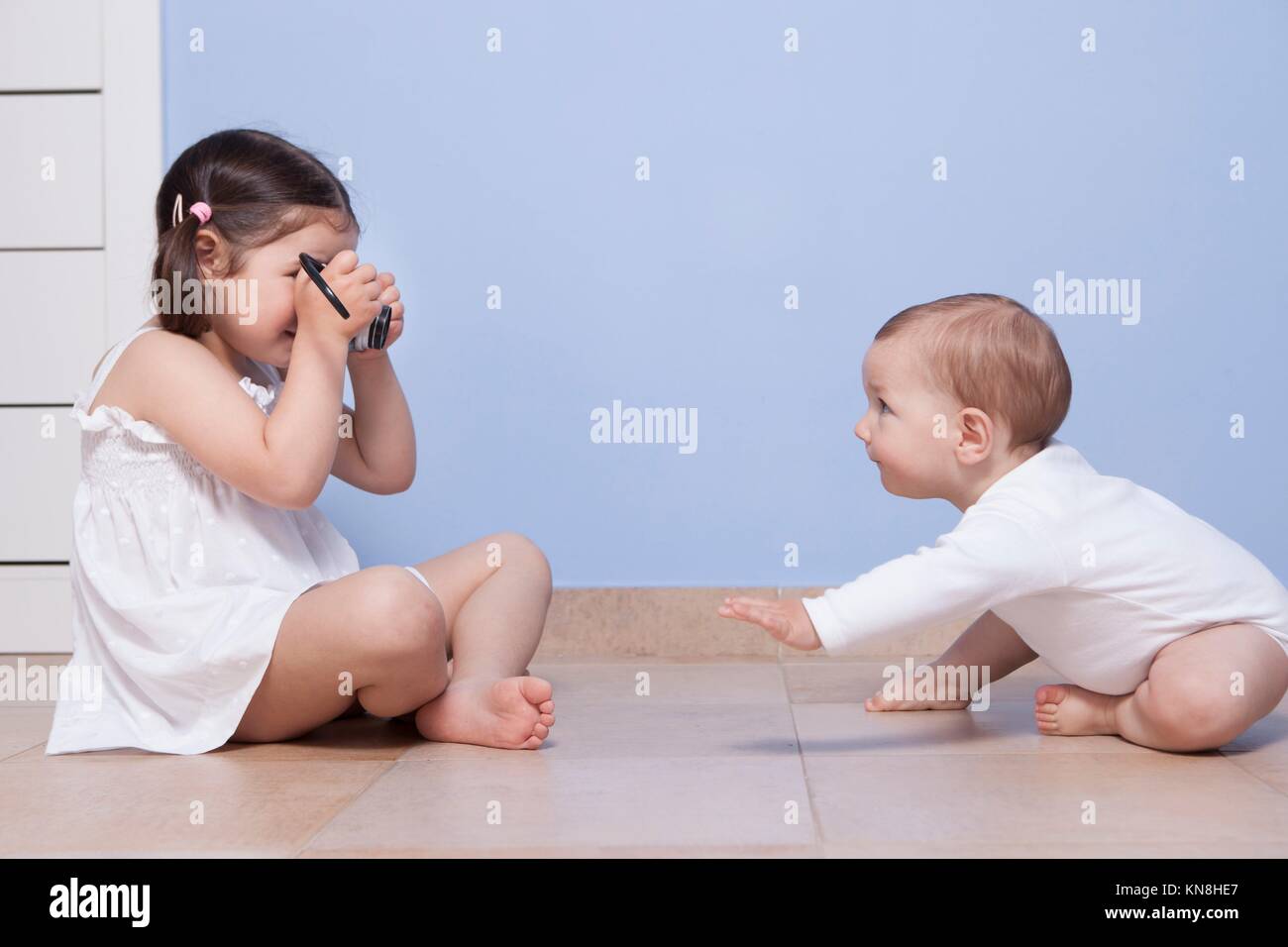 Young girl photographer. Pretty little sister taking pictures to her baby brother with old analog camera. Stock Photo