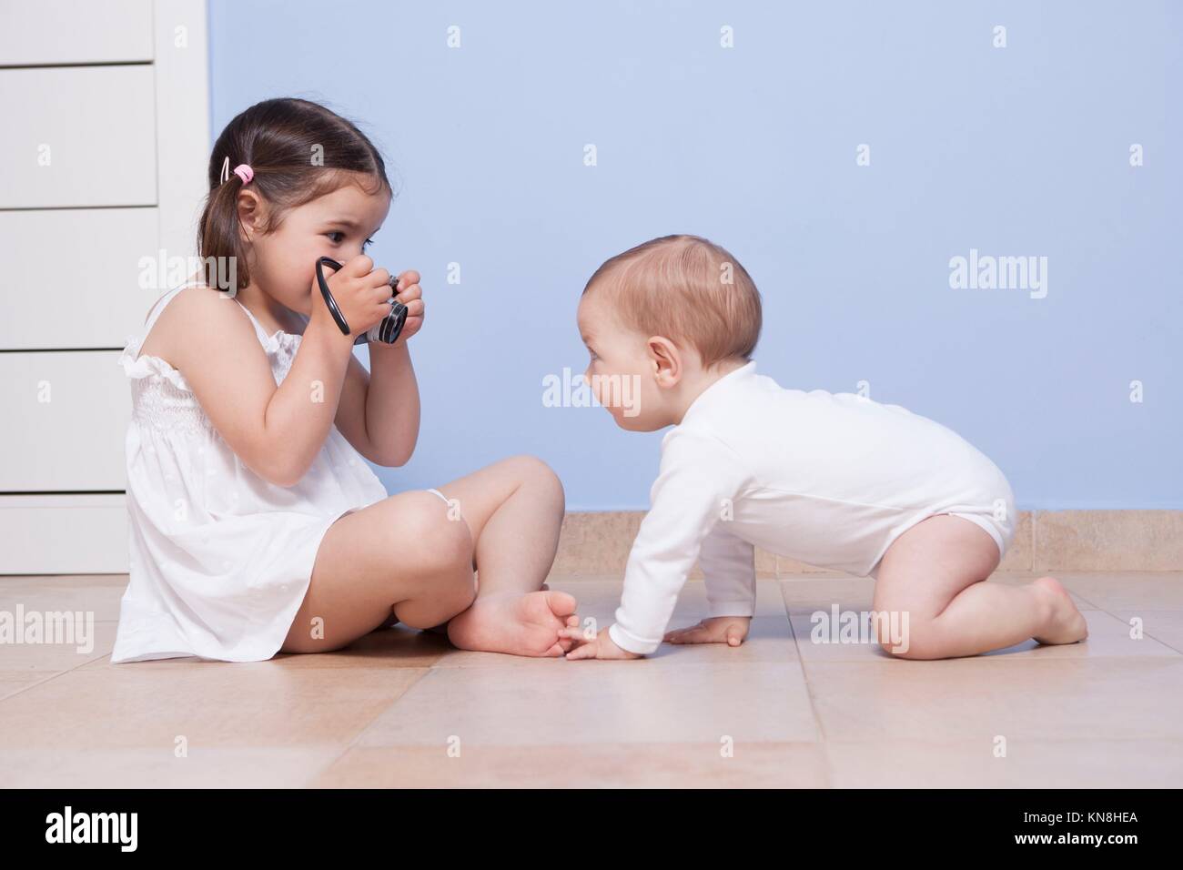 Young girl photographer. Pretty little sister taking pictures to her baby brother with old analog camera. Stock Photo