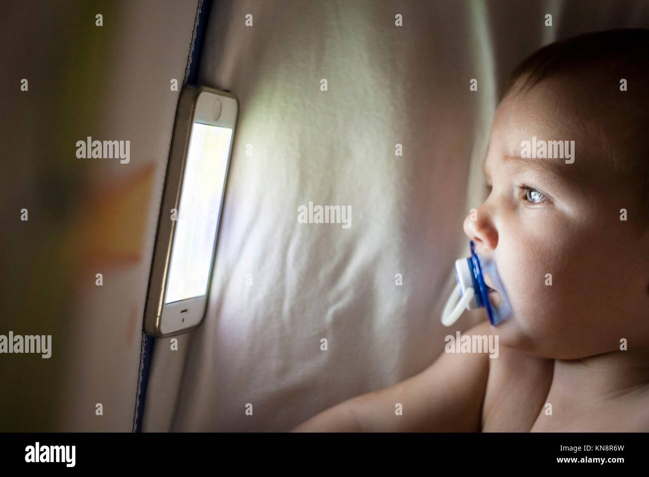 12 month old baby watching a lullaby cartoons with mobile phone on the crib. Stock Photo
