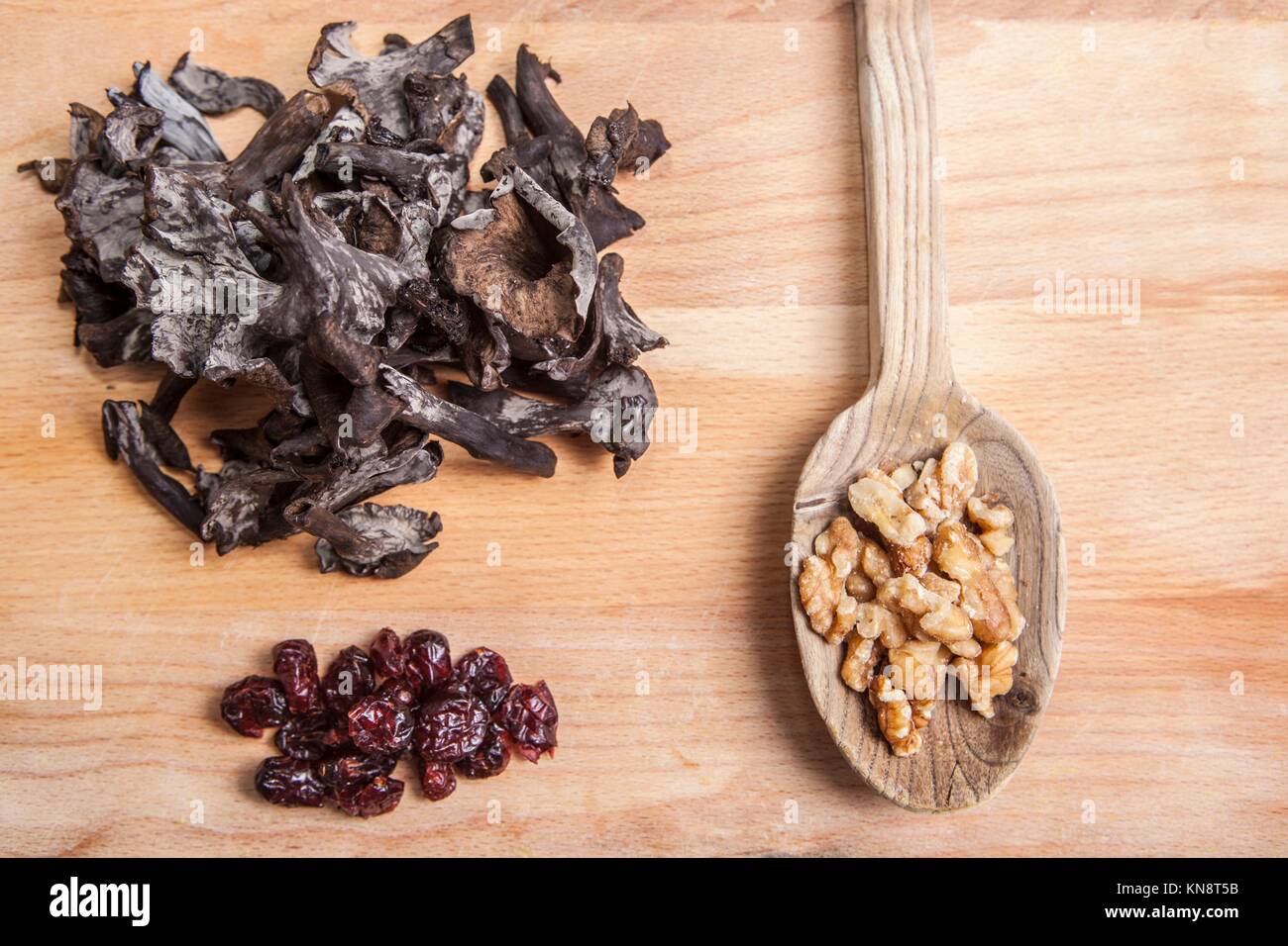 Horn of Plenty mushrooms. over chopping board with wooden spoon full of walnut and blueberry. Stock Photo
