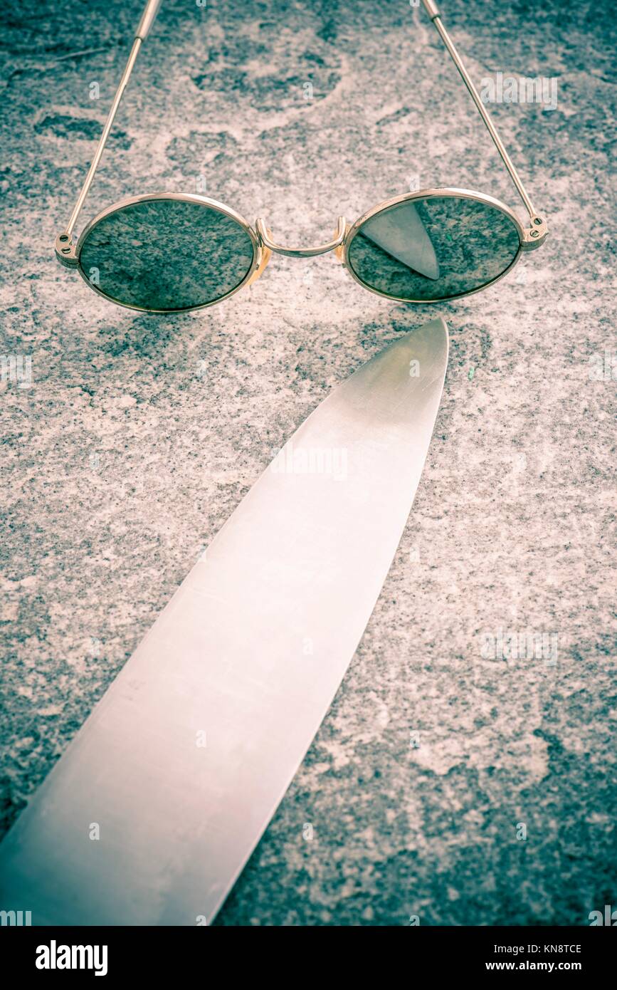 Round sunglasses and big knife on stone table, Retro eyewear. Concept of mystery, danger and fear. Stock Photo