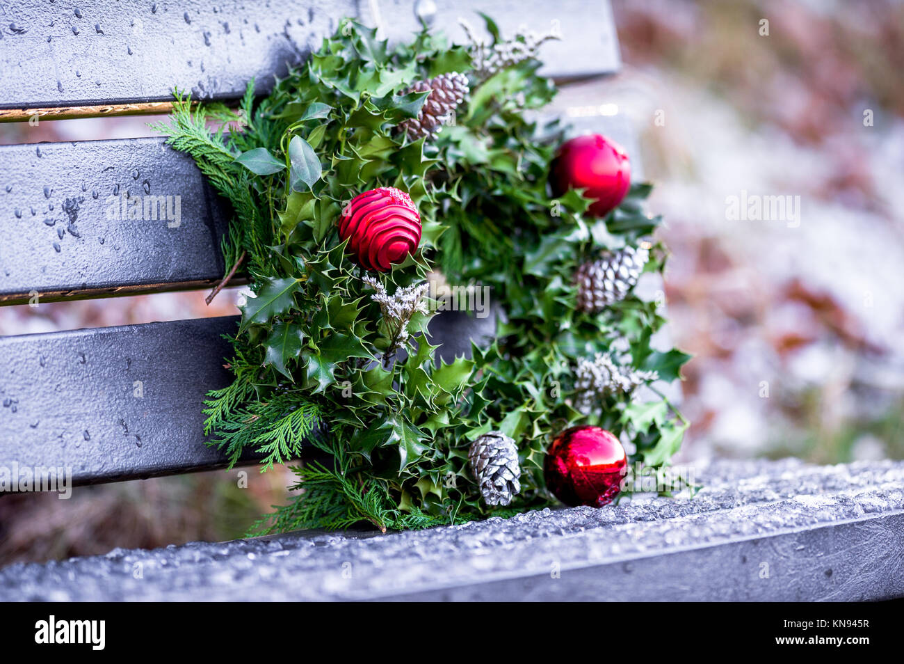 Decorative Christmas wreath made from pine and green holly leaves and red baubles laying a park bench. Stock Photo