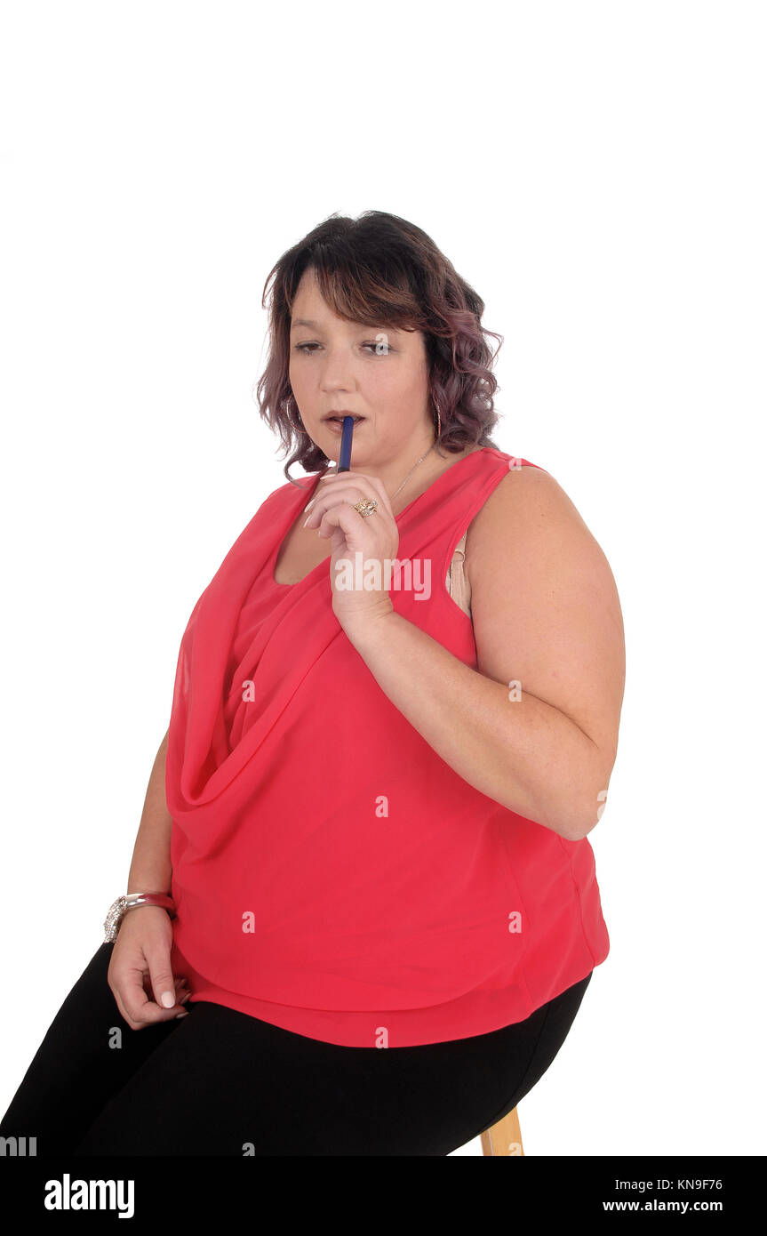 A lovely oversized woman in a red blouse sitting on a chair with her pen in her mouth, thinking, isolated for white background Stock Photo