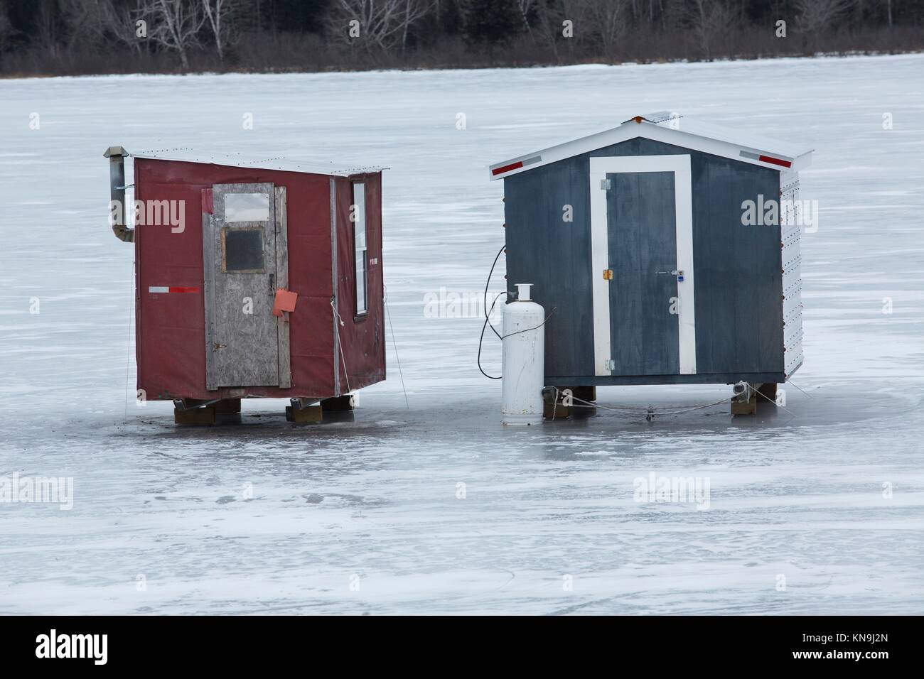Two red and gray ice fishing shelters sit side by side on the ice