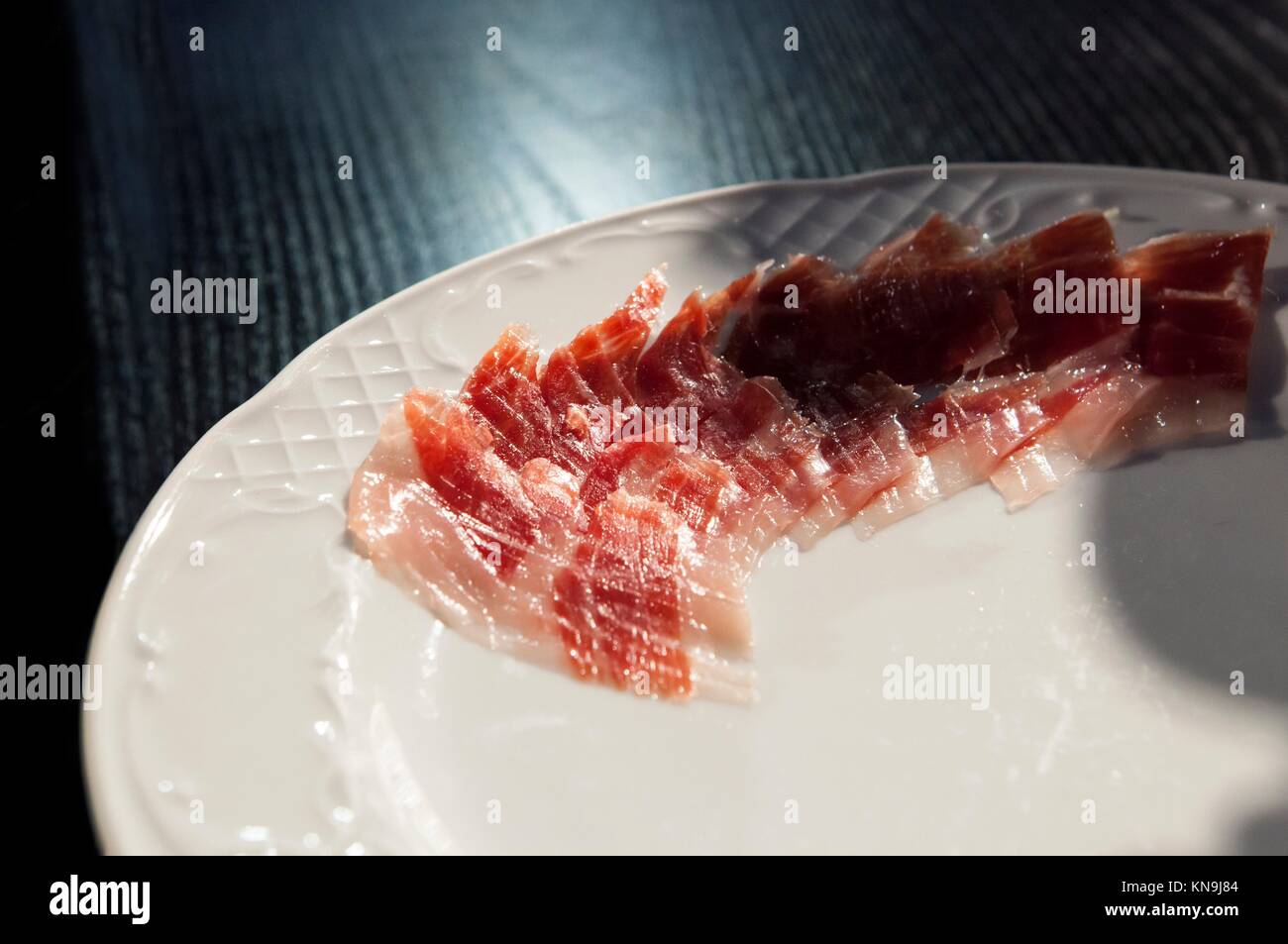 Half decorated arrangement of iberian cured ham on plate over black wooden background. Stock Photo