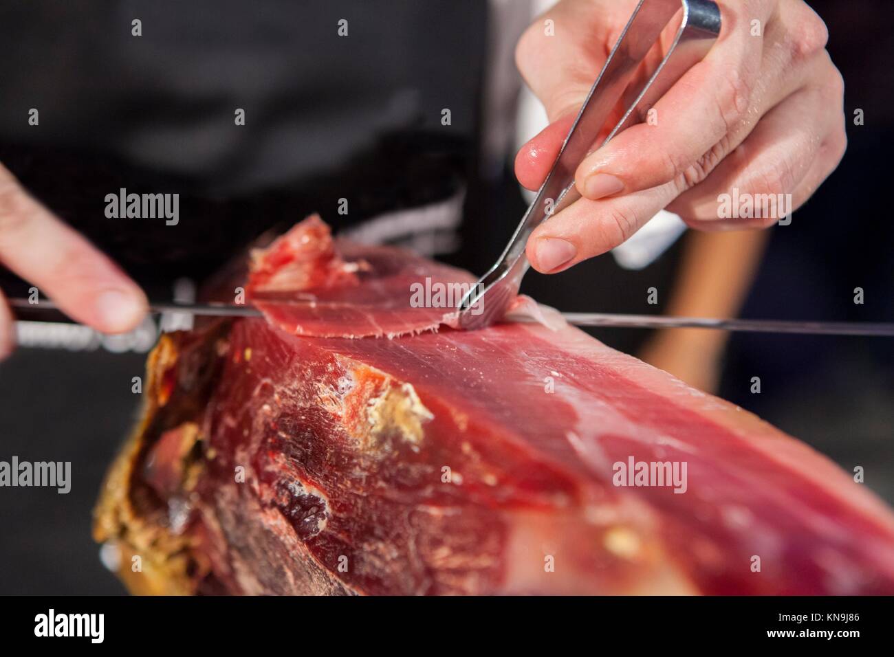 Master slicer cutting iberian cured ham. He is taking the slices with tongs. Stock Photo