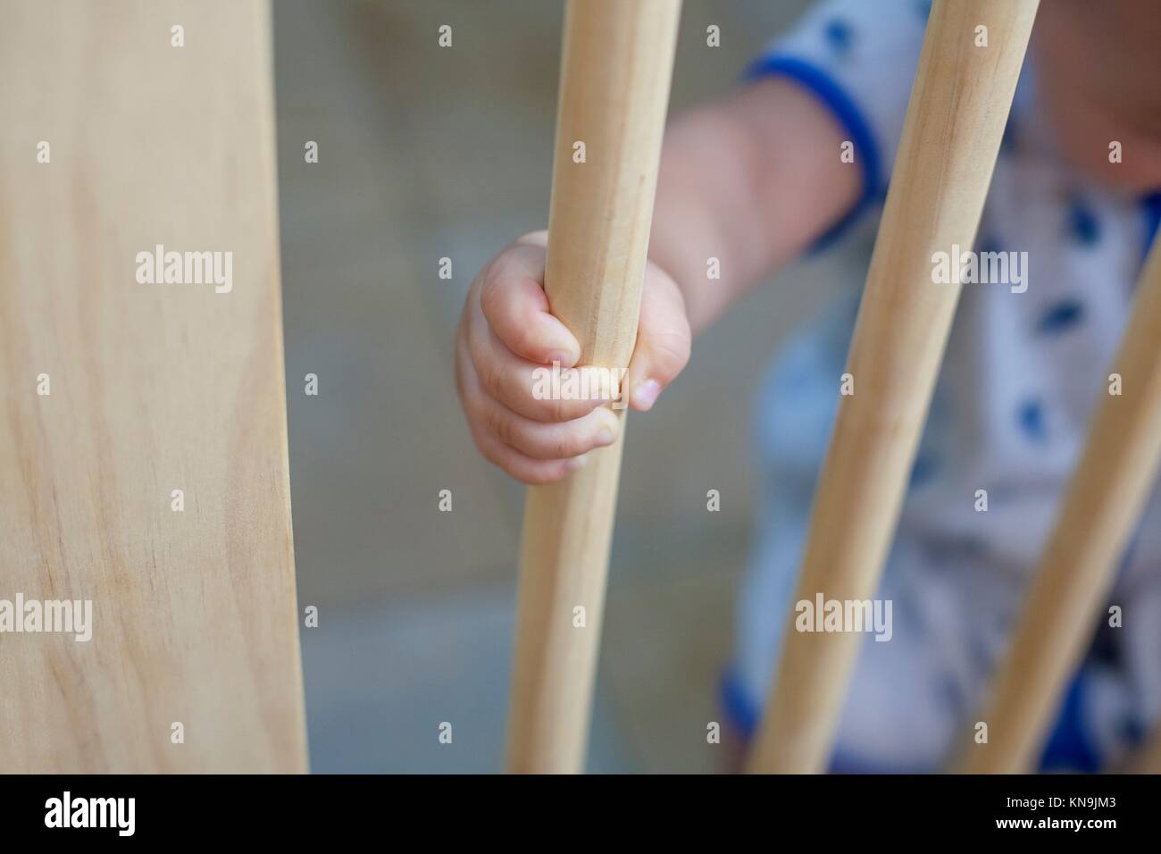 One year old baby boy behind the wooden safety gate of stairs. He is trying to go upstairs. Stock Photo