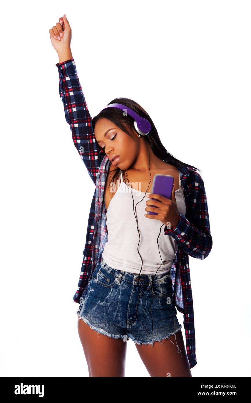 Beautiful teenager girl listening, dancing and jamming to music on mobile phone wearing purple headphones, on white. Stock Photo