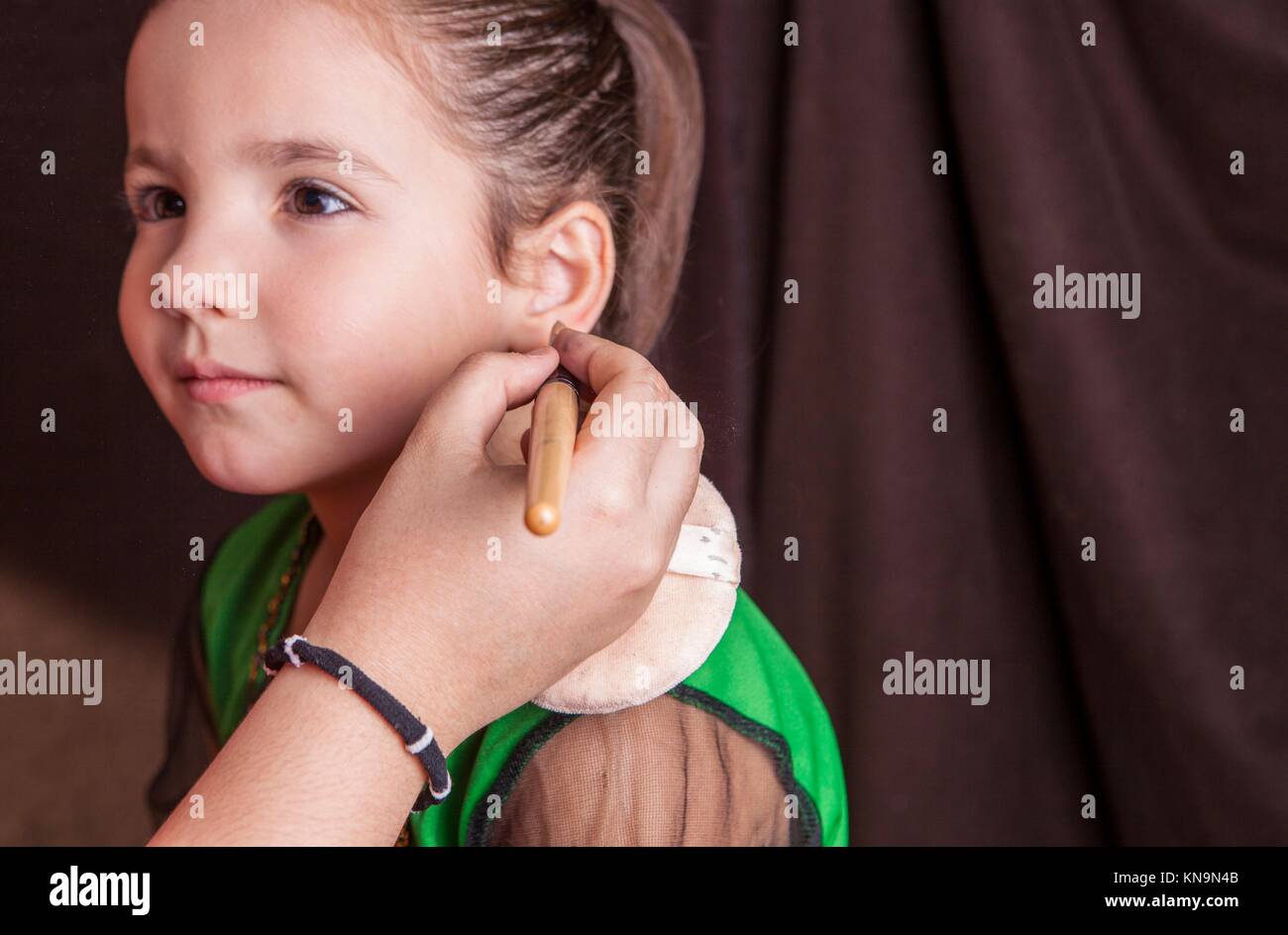 Little cute girl making facepaint before halloween party. The make-up artist is applying some foundation. Stock Photo