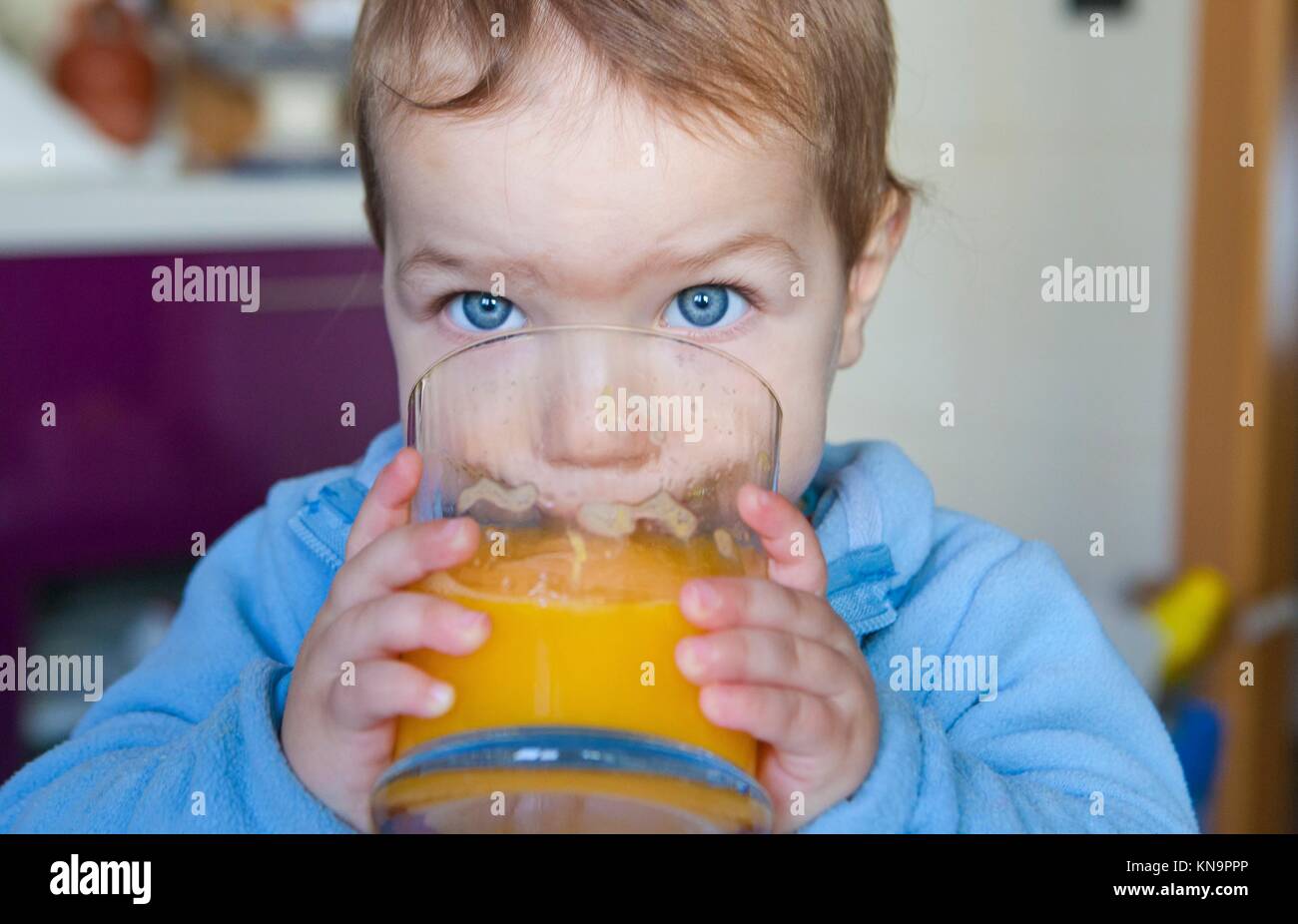 Baby boy drinking a big glass of orange juice fresh made. Education on healthy nutrition for children concept. Stock Photo