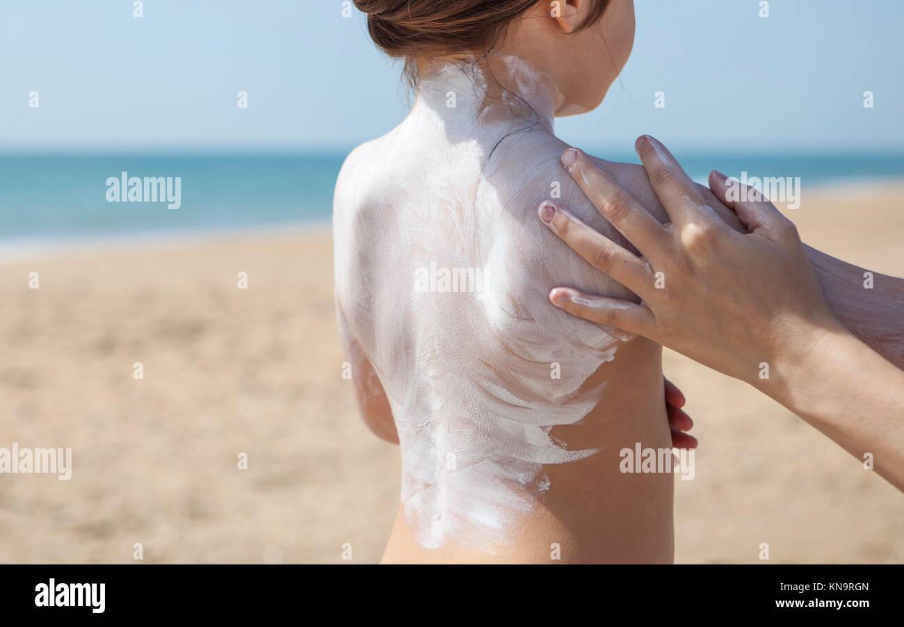 Mother applying sunblock cream to her daughter on shoulder, El Rompido, Huelva, Spain. Stock Photo