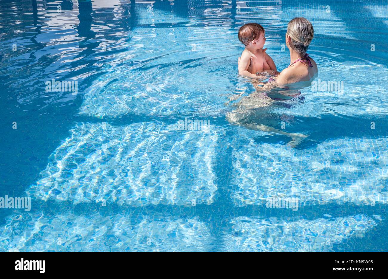 Mother playing with her baby at swimming pool indoor. Kids learn to swim during family vacation. Stock Photo