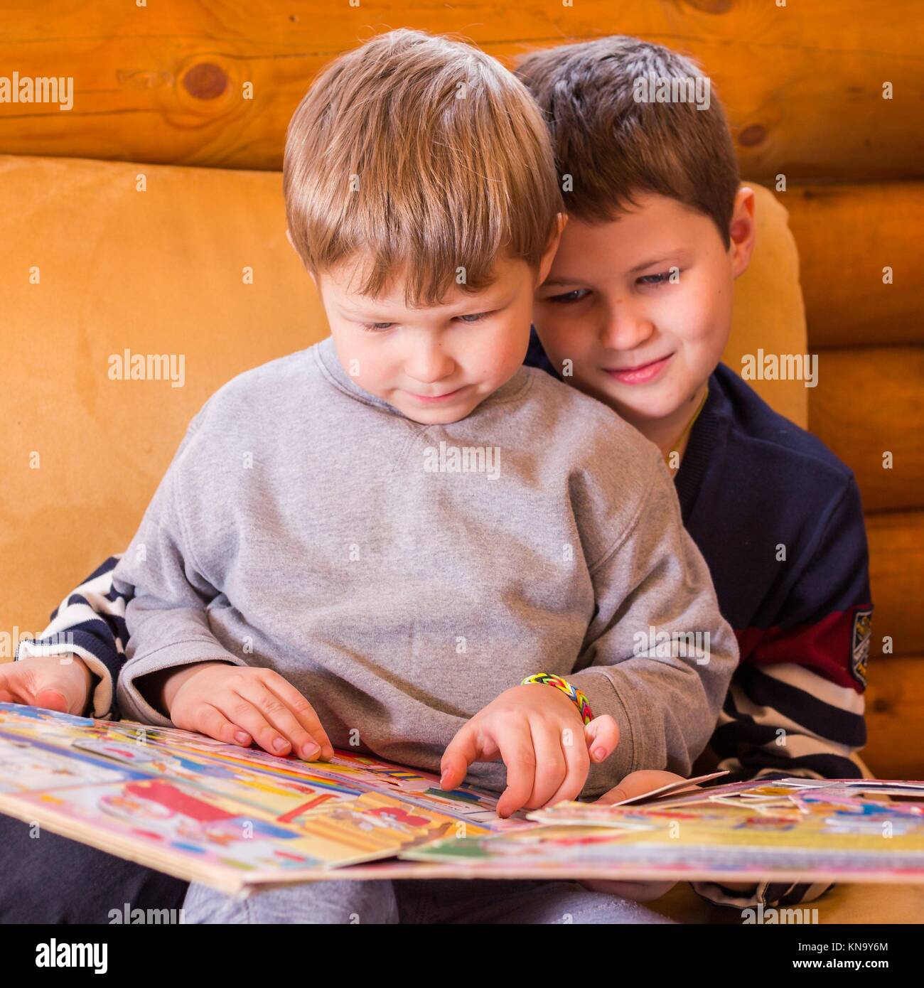 Younger brother learning to read with help of elder one. Stock Photo