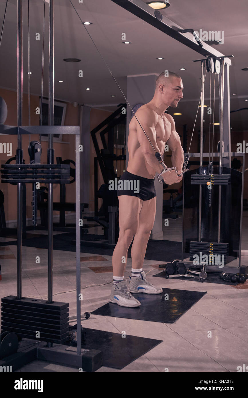 one bodybuilder, Multi-Station Gym Machine, cable pulling, full body lenght shot. Stock Photo