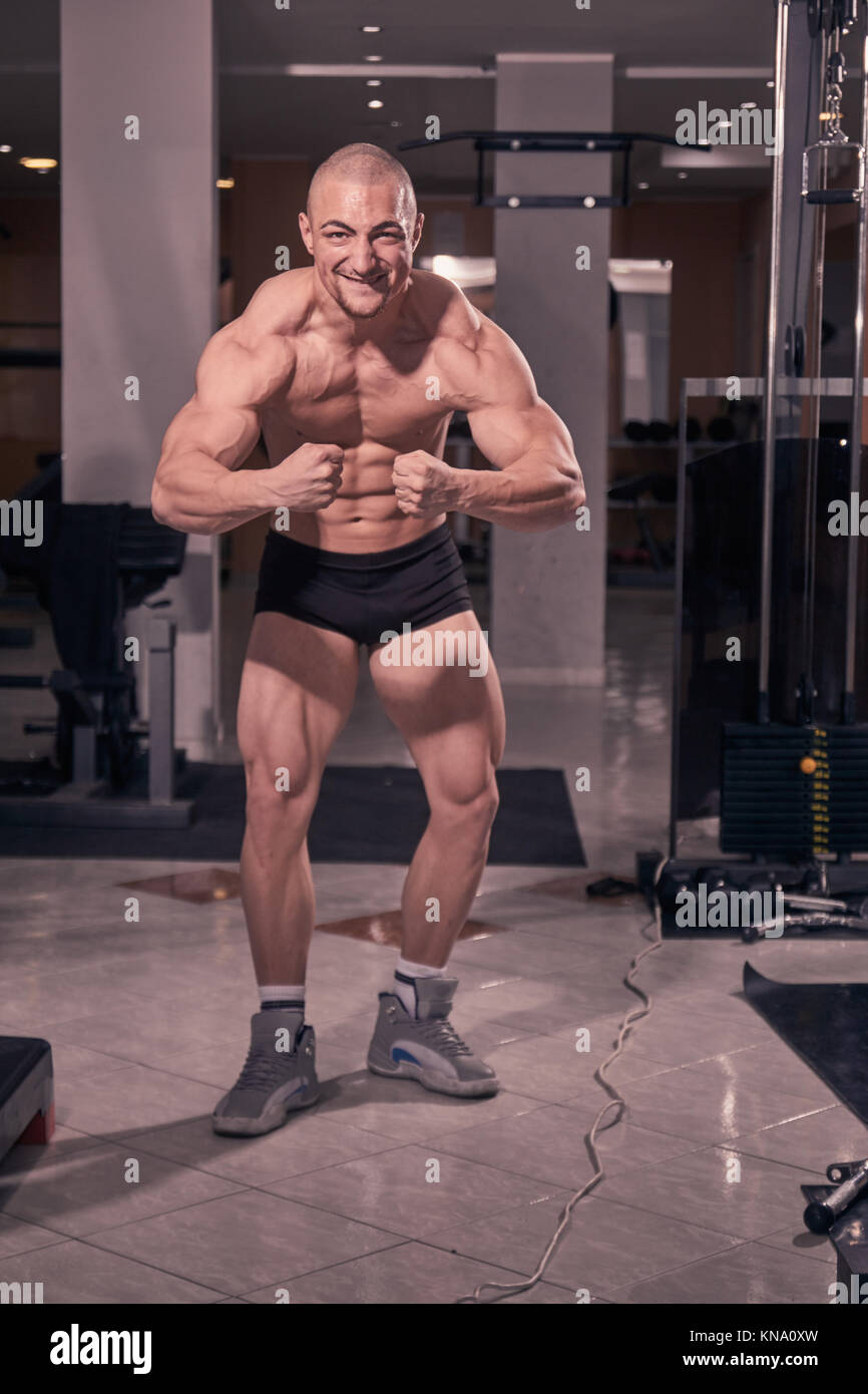 one young bodybuilder posing tough tense, gym interior. full lenght body shot. Stock Photo