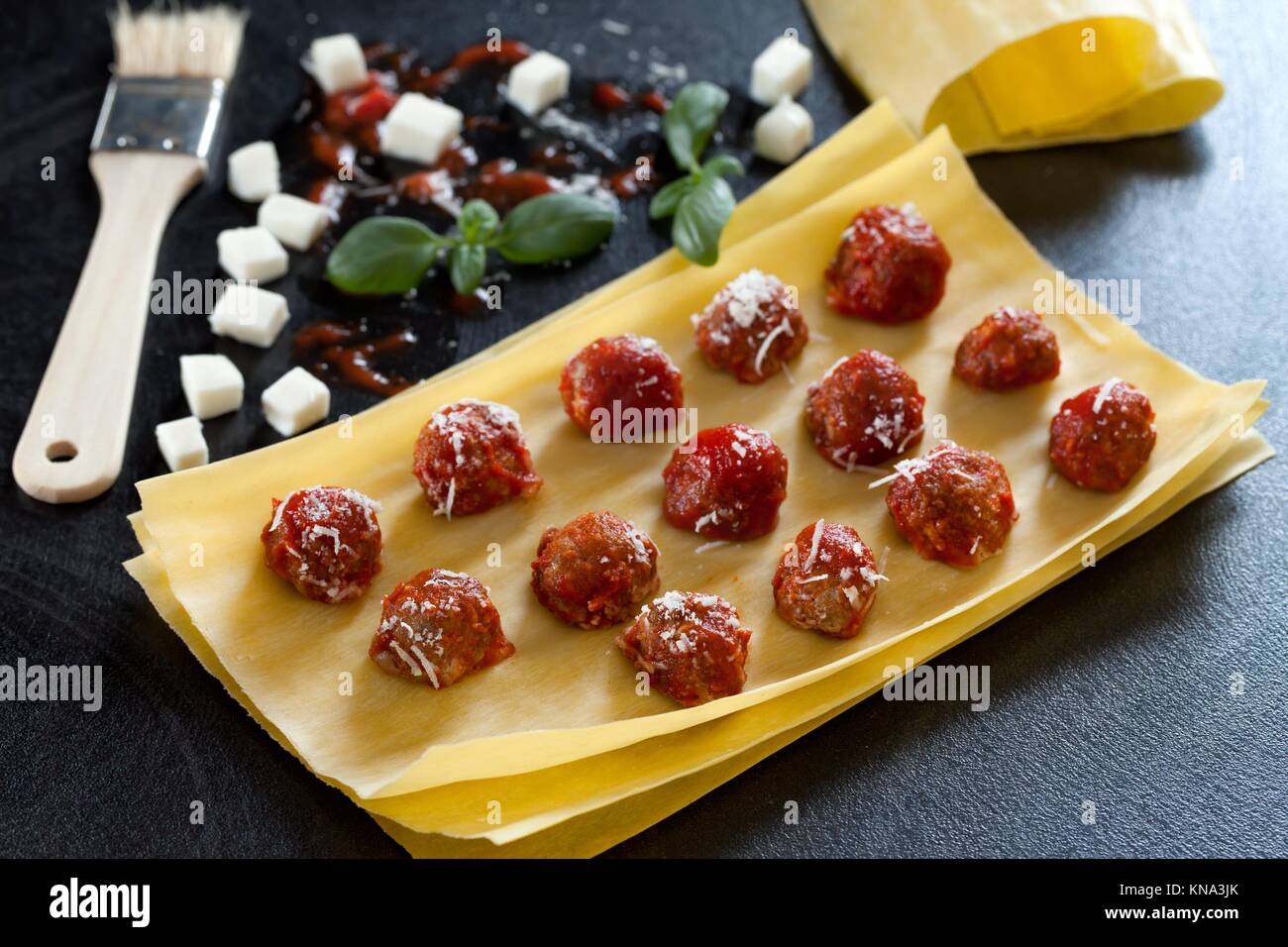 Closeup of raw lasagna sheets with small meatballs in tomato sauce
