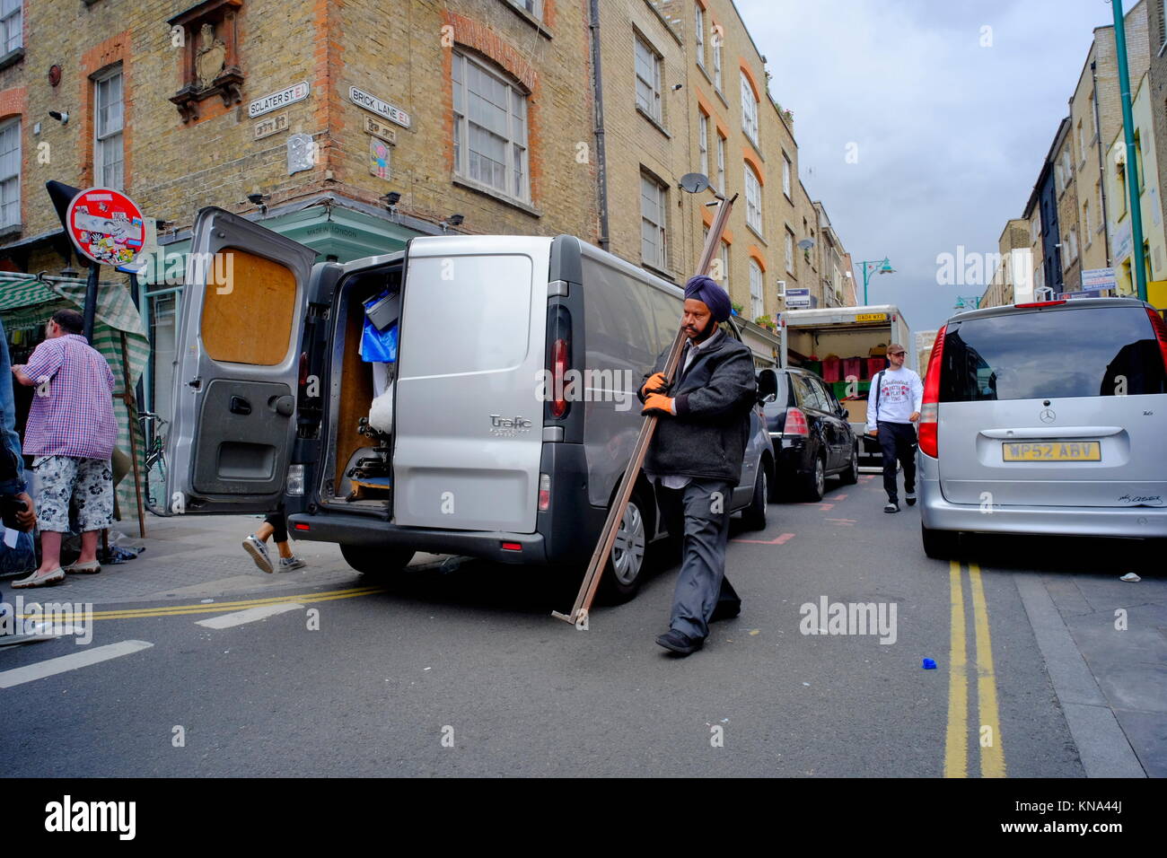 Sikh man carrying metal poles to a silver van in Shoreditch, London, England, UK Stock Photo