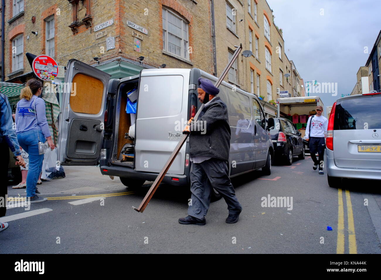 Sikh man carrying metal poles to a silver van in Shoreditch, London, England, UK Stock Photo