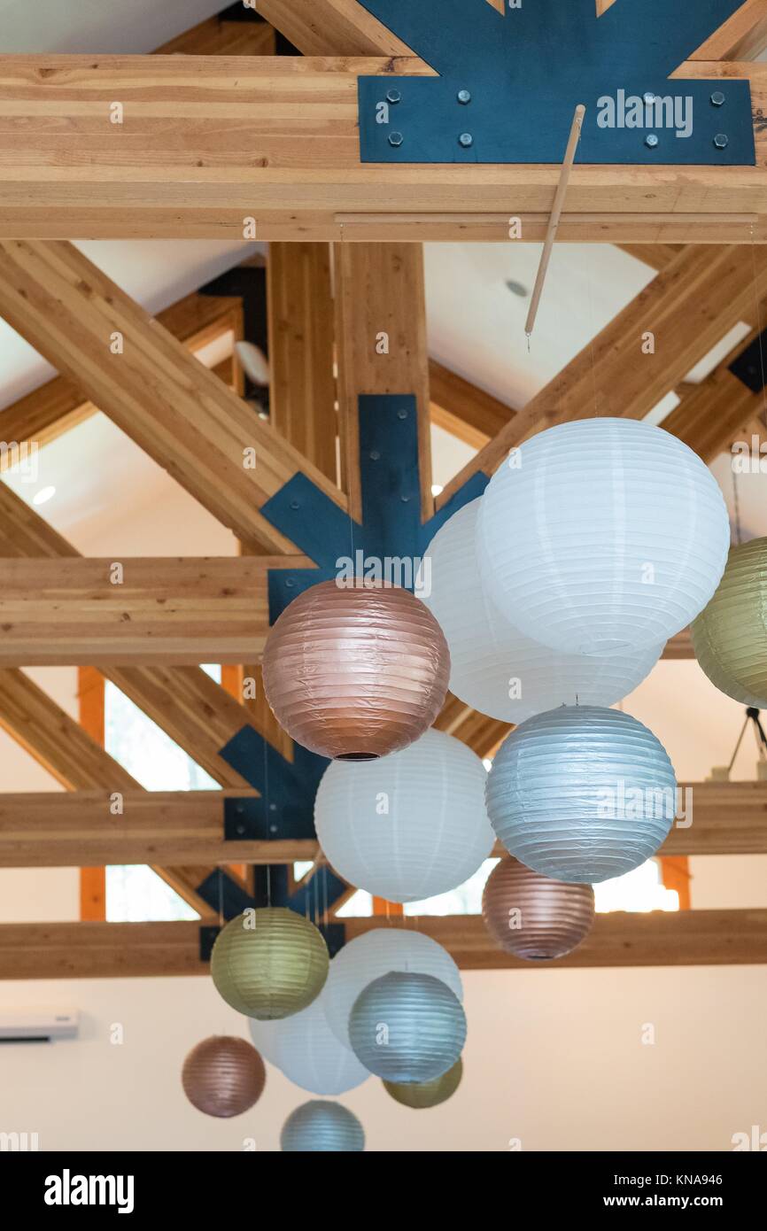 Wedding reception decor of white, gold, and silver paper lanterns hung high in the rafters at a wedding venue. Stock Photo