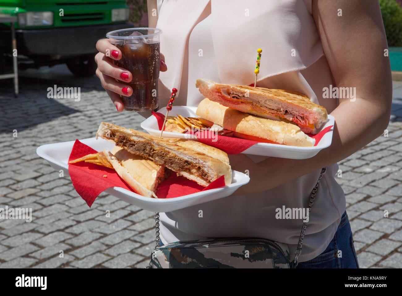 Girl with trays full of meal from food truck trailer. She is got meat pie. Stock Photo