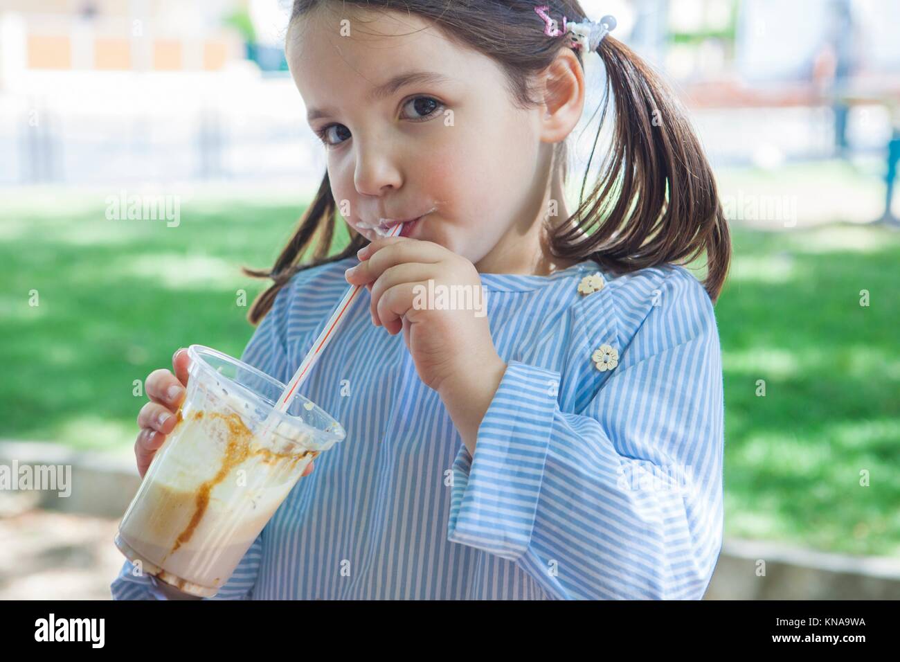 Little girl drinking milkshake at park. She is 5 years old. Stock Photo