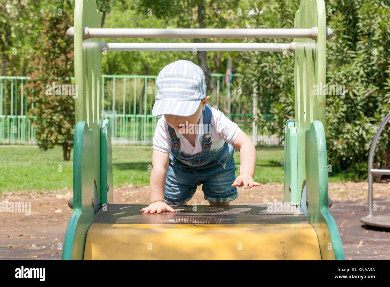 2 year-old boy reaching to the top of slider at playground. Tenacity concept. Stock Photo