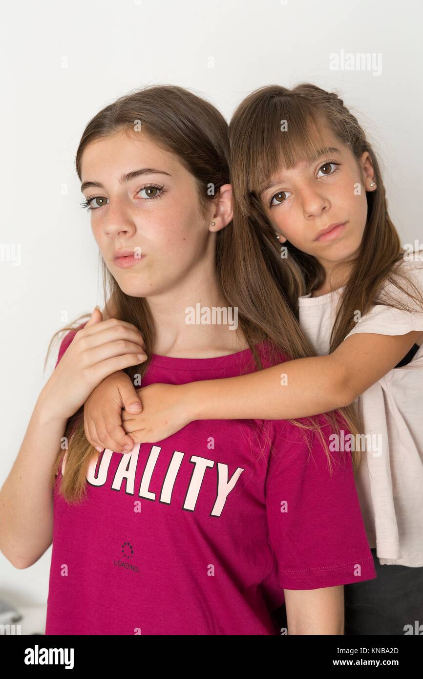 Portrait of two 15 and 10 year old sisters on a white background. It takes with natural light that enters through a window. Stock Photo
