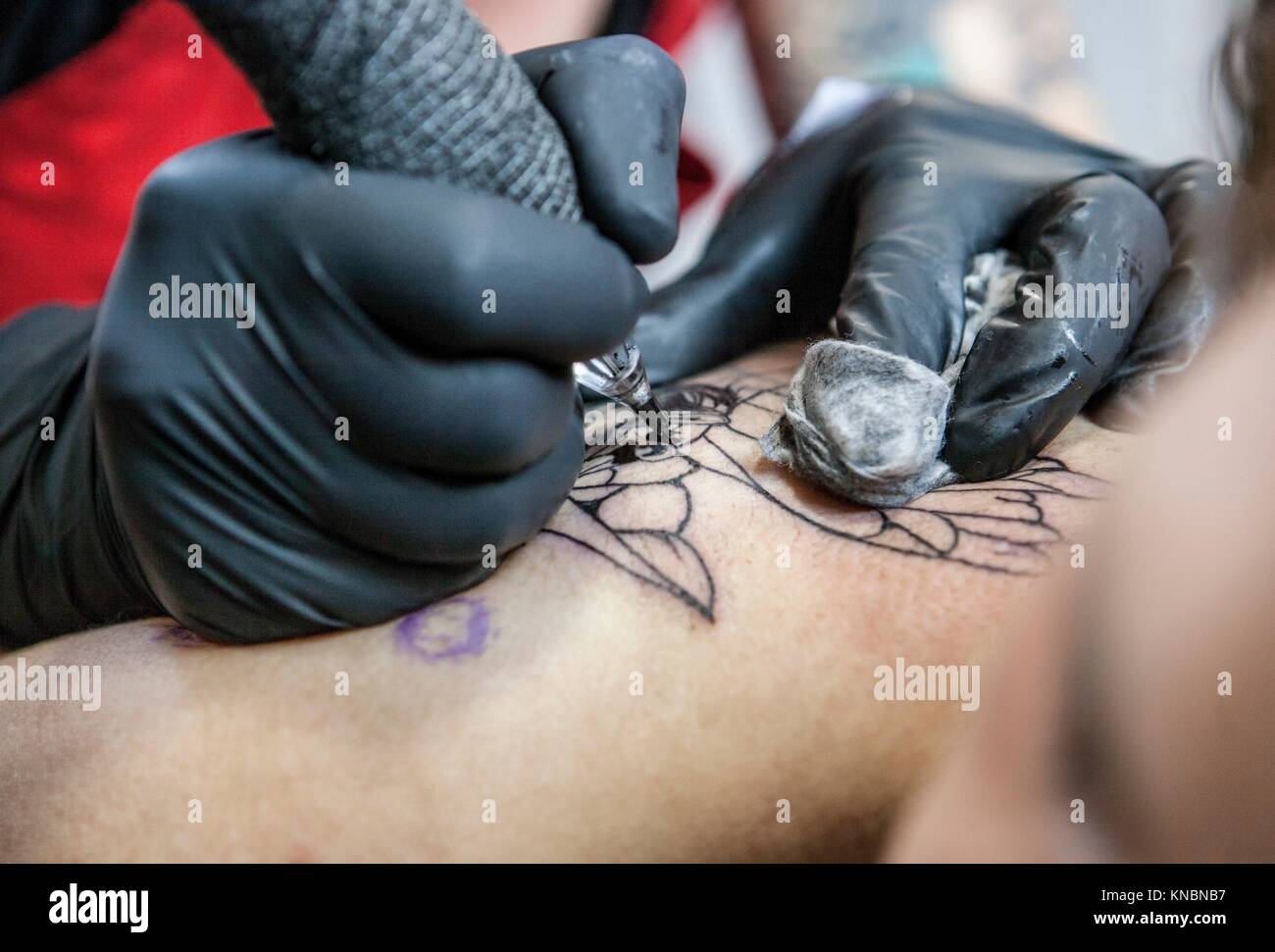 Tattoo artist applies tattoo to shoulder blade of a woman. She is outlining the tattoo. Stock Photo