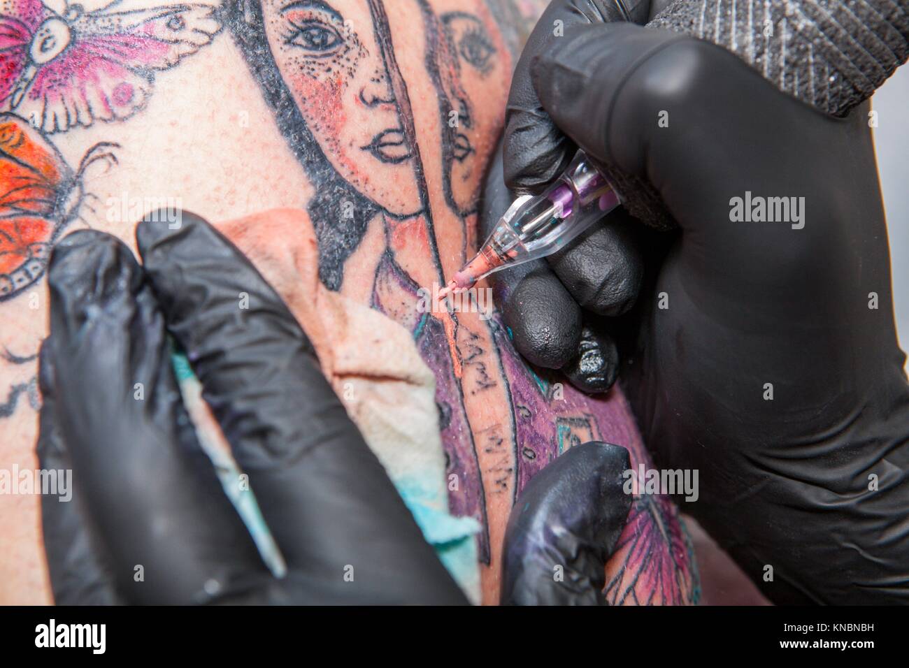 Tattoo artist applies tattoo to arm. She is filling with flesh-coloured ink the tattoo. Stock Photo