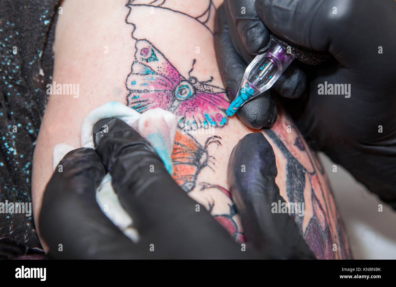 Tattoo artist applies tattoo to arm. She is filling with light blue color the tattoo. Stock Photo