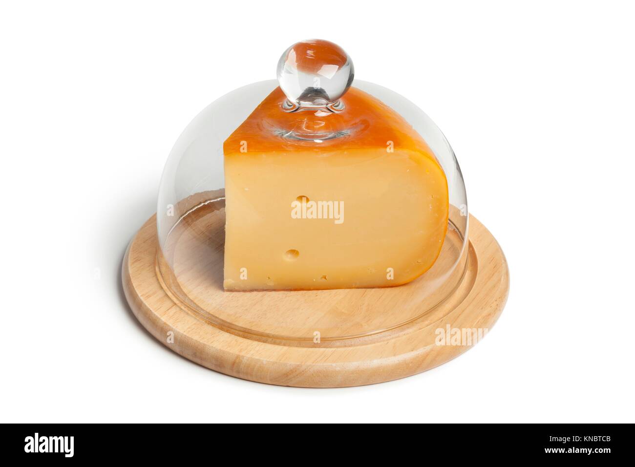 Piece of Dutch Gouda cheese on a wooden board covered with a glass hood.