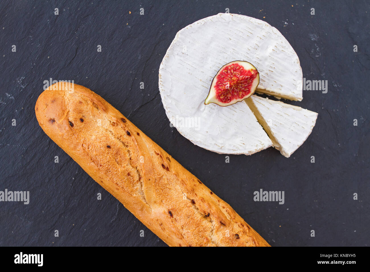 Bright juicy ripe piece of fig fruit and creamy Swiss camembert cheese and a crispy golden fresh onion baguette for breakfast on graphite background. Stock Photo