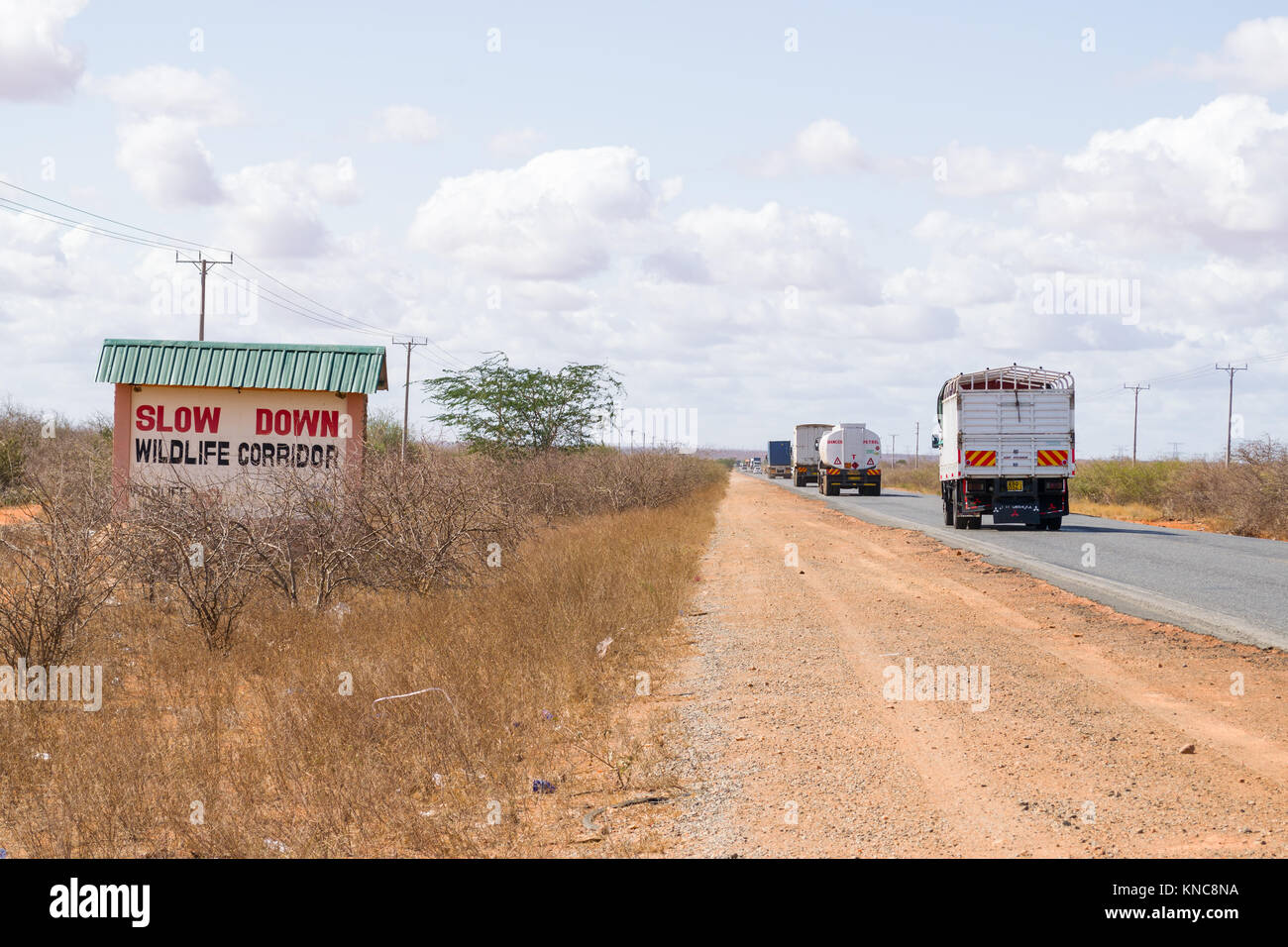 Trucks and other vehicles driving on the Mombasa road past a sign that advises the area is a wildlife corridor, Kenya, East Africa Stock Photo