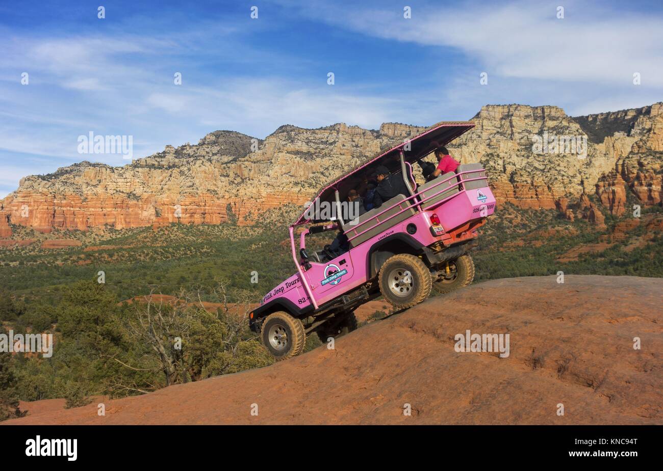 Pink Jeep Off Road High Clearance Terrain Vehicle touring Broken Arrow Slick Rock Desert Landscape with Tourists onboard near Sedona Arizona Stock Photo