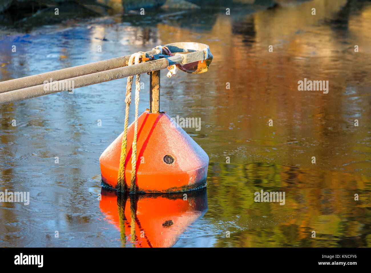 Bright orange marina mooring buoy in water with very thin ice. Some